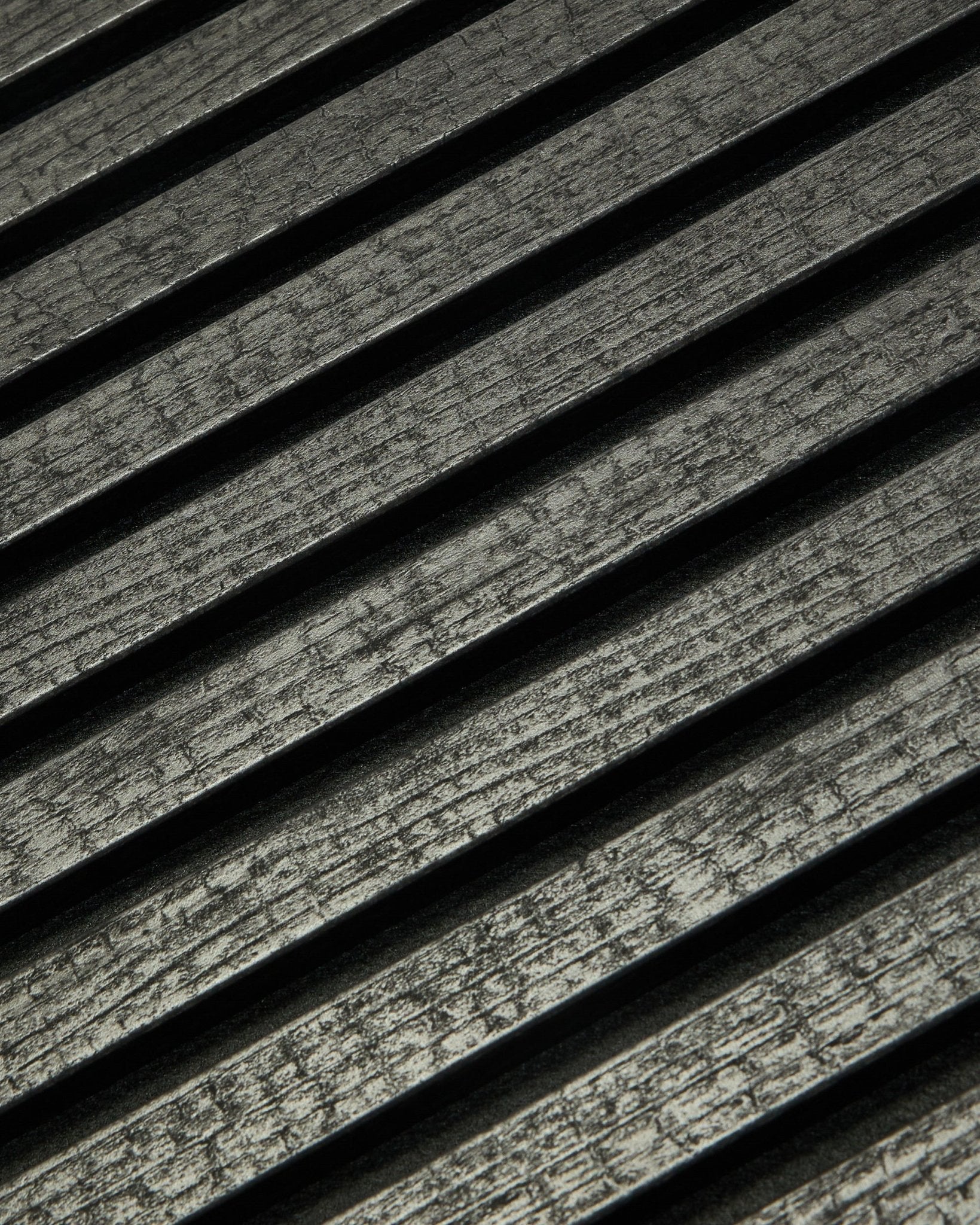 Gros plan sur le WoodUpp Rebel Akupanel en Charcoal (240x60 cm), montrant black, des lattes acoustiques rainurées disposées en diagonale pour une meilleure absorption sonore.