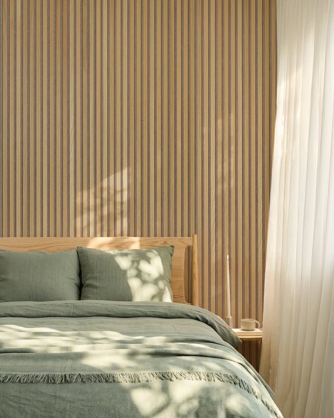Chambre nordique minimaliste avec un mur en chêne WoodUpp Akupanel Panneau acoustique, du linge de lit vert sauge, un cadre de lit en bois et des rideaux blancs vaporeux.