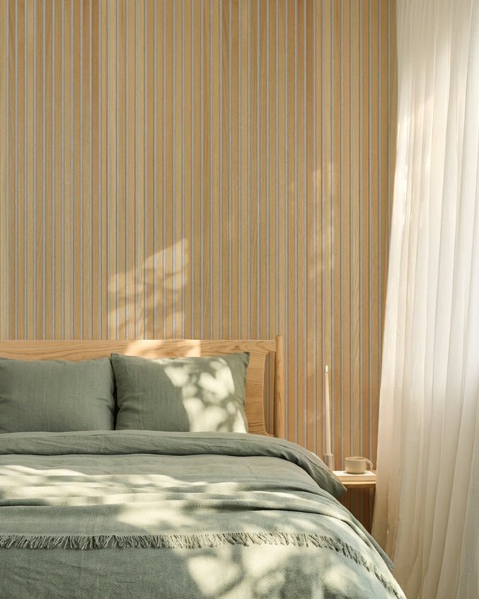 Chambre nordique minimaliste avec linge de lit vert sauge et mur acoustique à lattes WoodUpp Classic Oak Akupanel ; la lumière du soleil crée de douces ombres sur le lit.