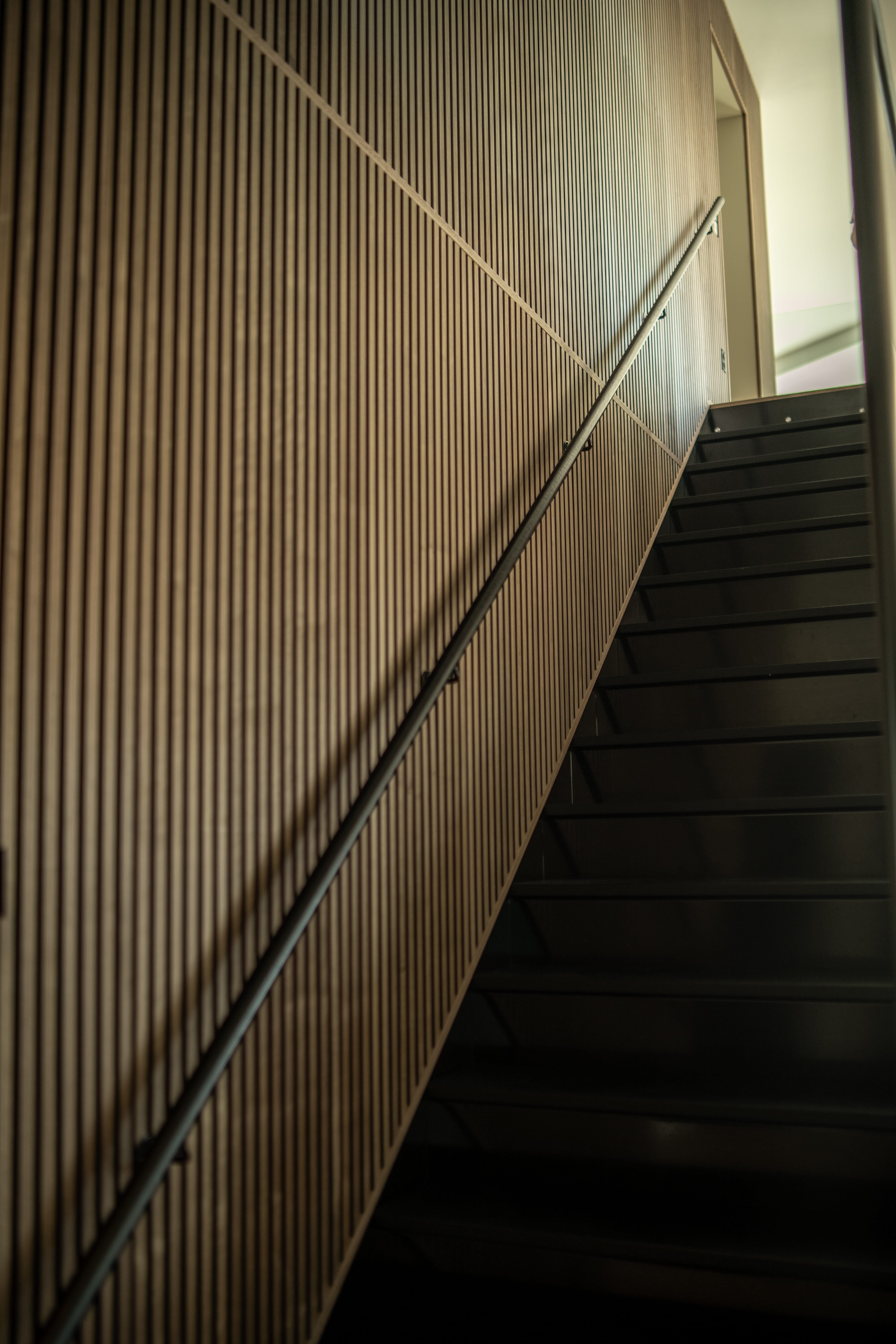Un escalier moderne aux marches noires est complété par un panneau acoustique vertical, vu den bas et de biais, pour un aspect nordique minimaliste.