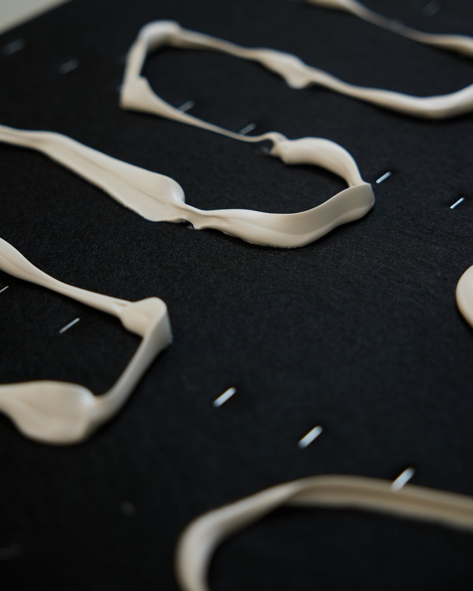 Lignes ondulées crème-colored d’un matériau épais sur une surface black Panneau acoustique texturée, avec des agrafes métalliques small et des motifs abstraits sur toute la surface.