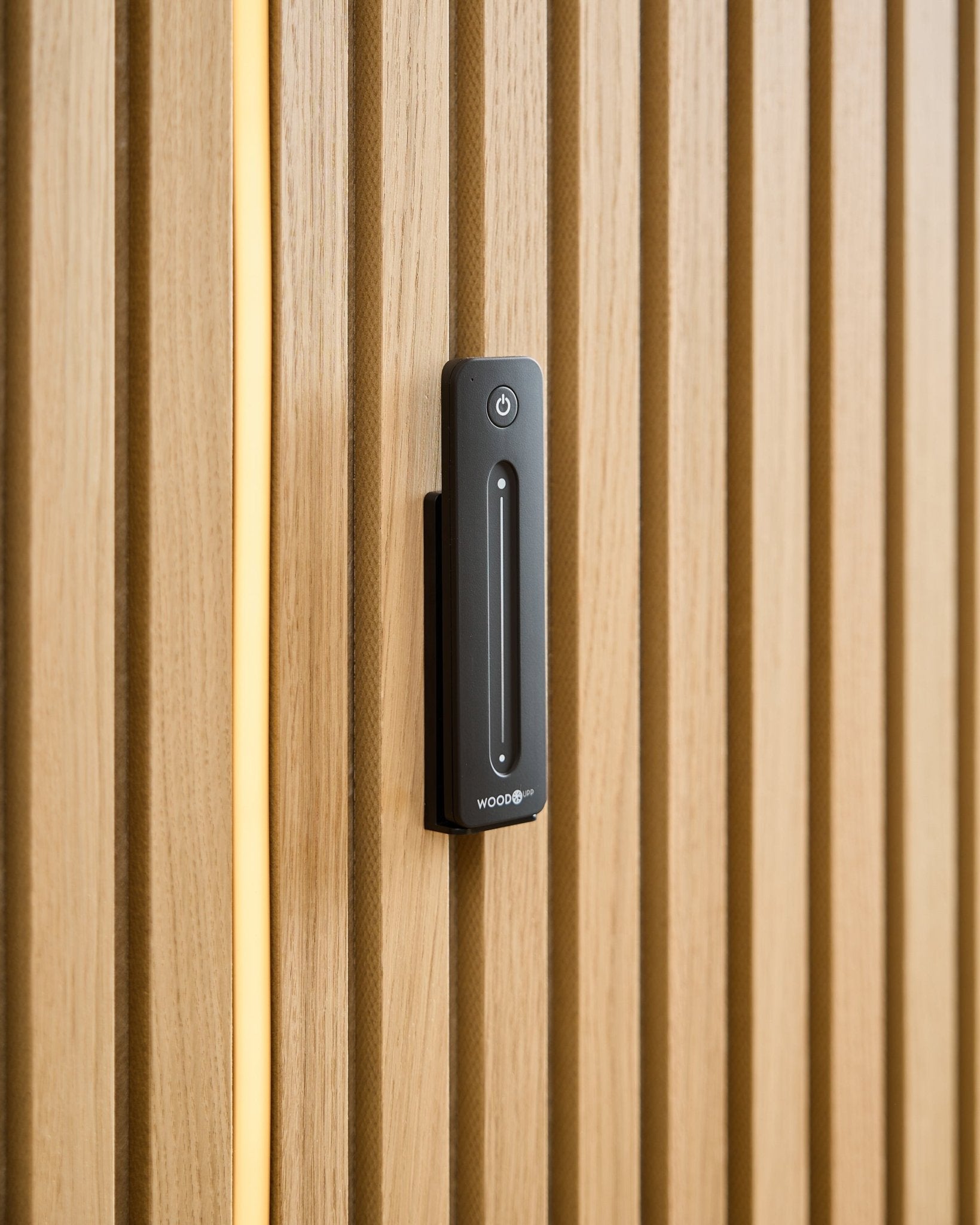 Un WoodUpp Lumi | Remote / LED Striplight est installé sur un Panneau acoustique en bois clair, avec un câble jaune visible derrière les lattes en bois.