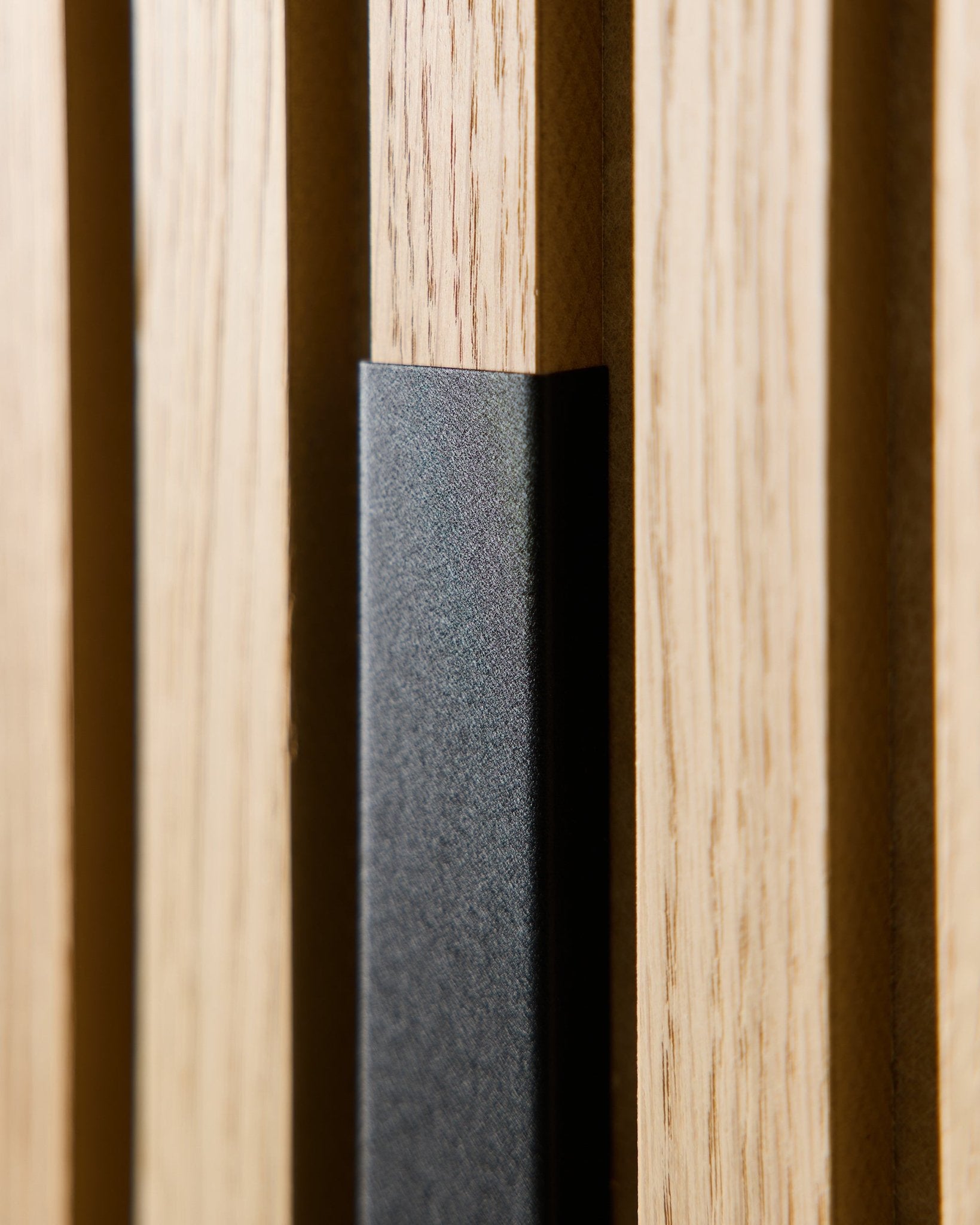 Gros plan sur le Liva Panneau acoustique de WoodUpp avec cache en aluminium black de 60 cm, mettant en valeur les lattes en bois vertical et une touche black pour des intérieurs nordiques modernes.