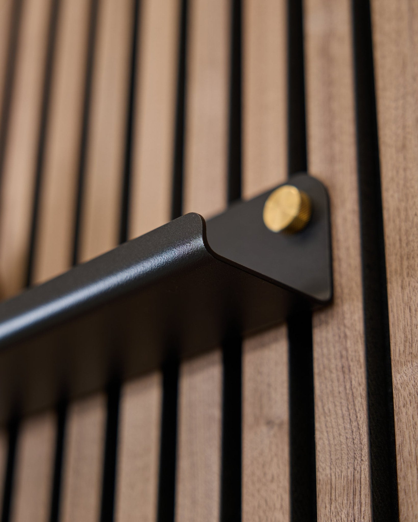 Gros plan sur la Norr | Narrow Shelf (75,9 cm) de WoodUpp en black, avec une poignée steel à boulons dorés et une surface acoustique à rainures verticales.