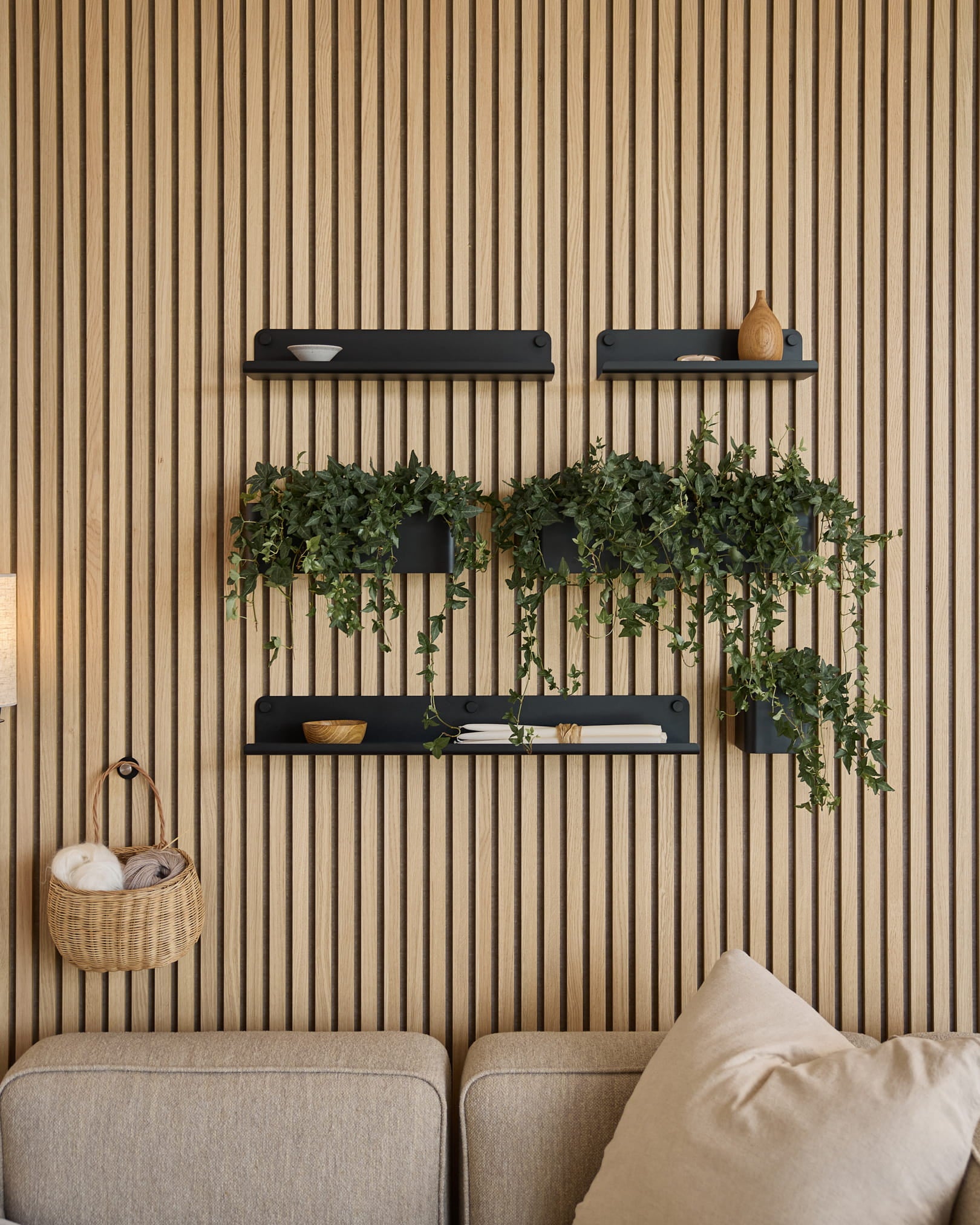 Salon contemporain avec un panneau acoustique nordique à lattes, des étagères black, des plantes retombantes dans le Plant Box Norr de WoodUpp (35.9 cm, Black) et un canapé beige.