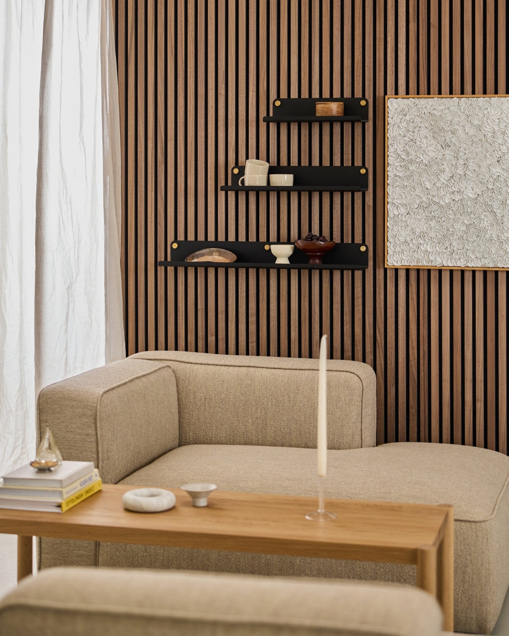 Salon moderne avec un canapé beige, une table en bois, une étagère large WoodUpp black Norr (51,9 cm) et un mur texturé Akupanel Panneau acoustique orné d’un art abstrait.