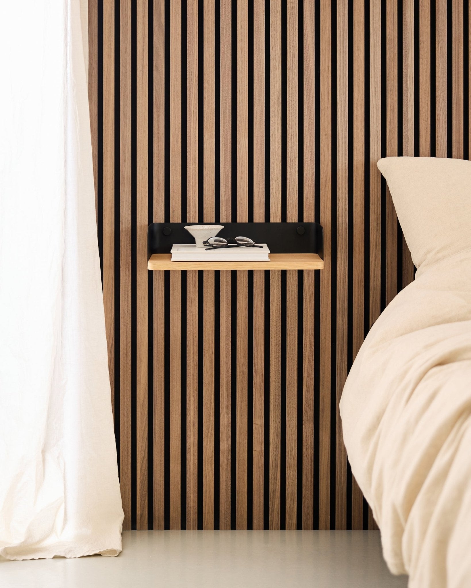 Chambre minimaliste avec un mur à lattes de bois nordique Panneau acoustique, la bibliothèque WoodUpp Linn en Natural Oak, et une table de chevet suspendue à côté d’un lit beige.