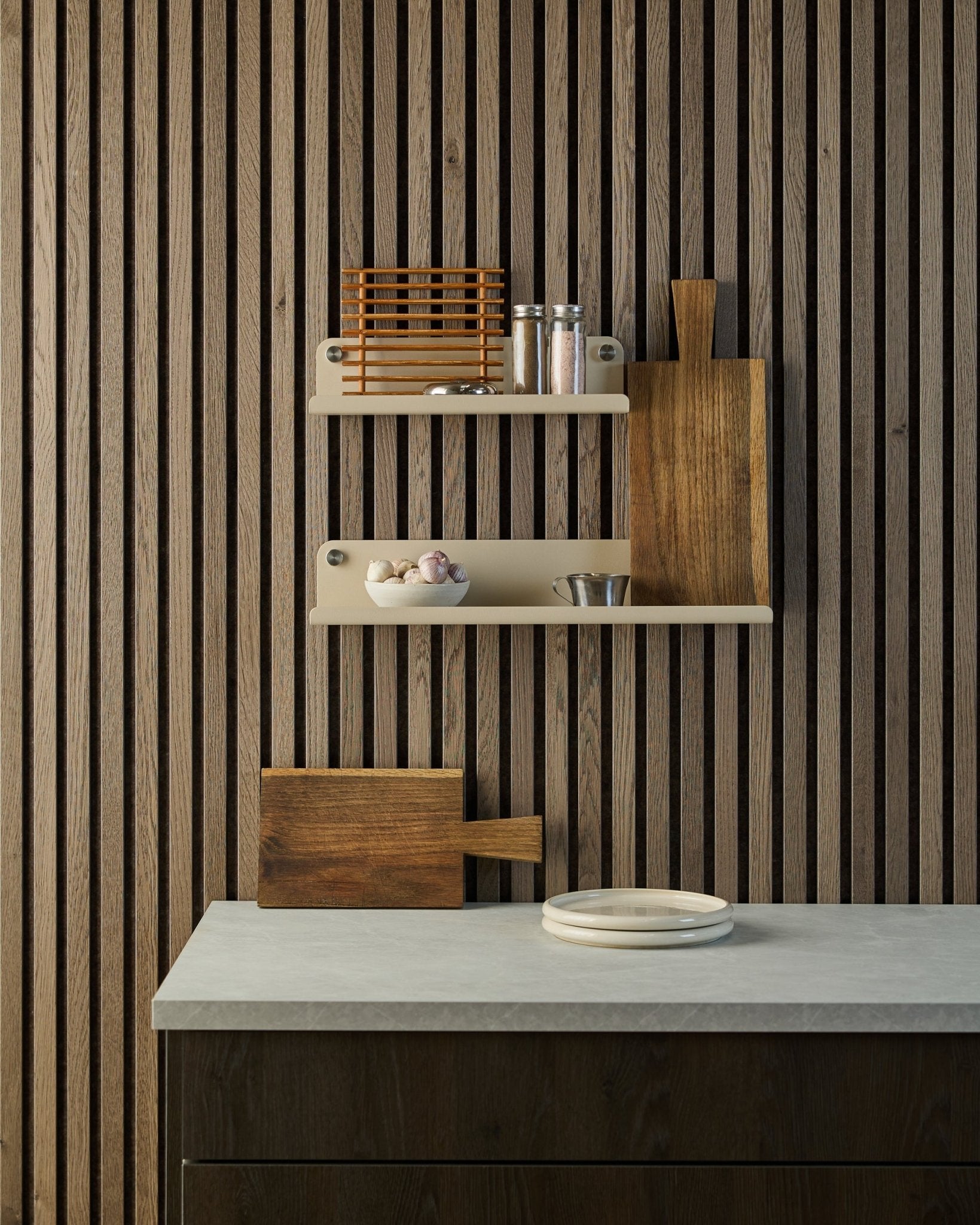 Cuisine minimaliste avec mur acoustique à lattes en bois nordique Akupanel, étagères ouvertes accueillant des épices et des bols, plan de travail avec assiettes blanches et planche à découper.