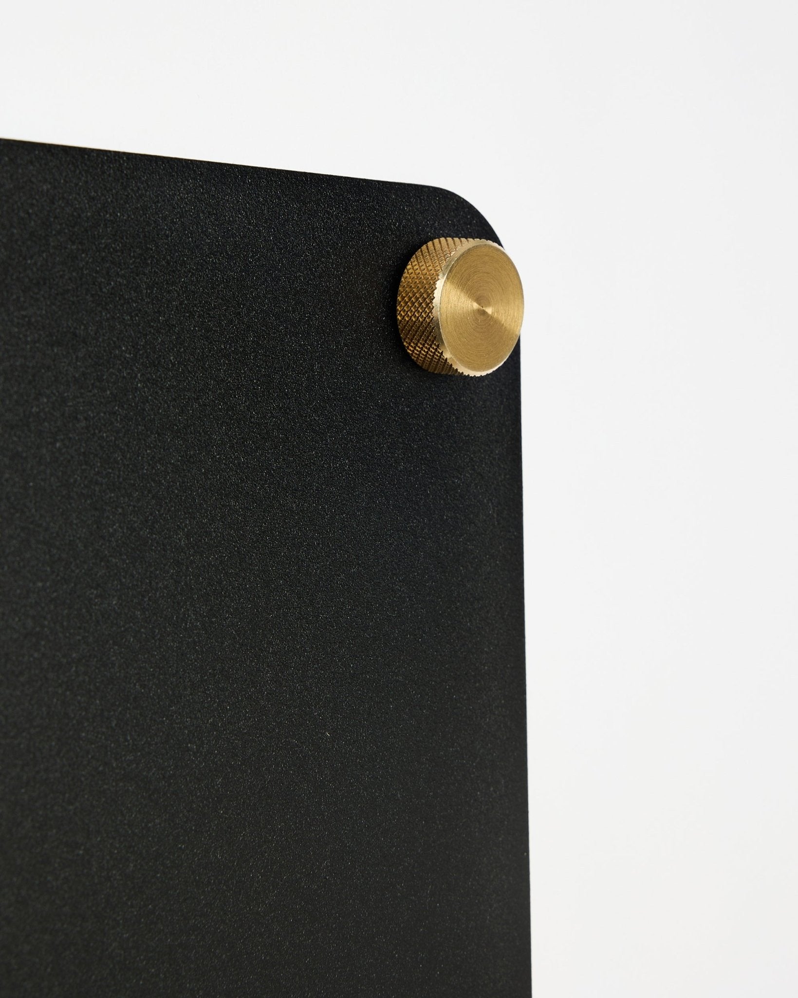 Gros plan sur le tableau magnétique acoustique WoodUpp Norr black (small), avec un coin arrondi et une fixation à vis dorée sur fond blanc.