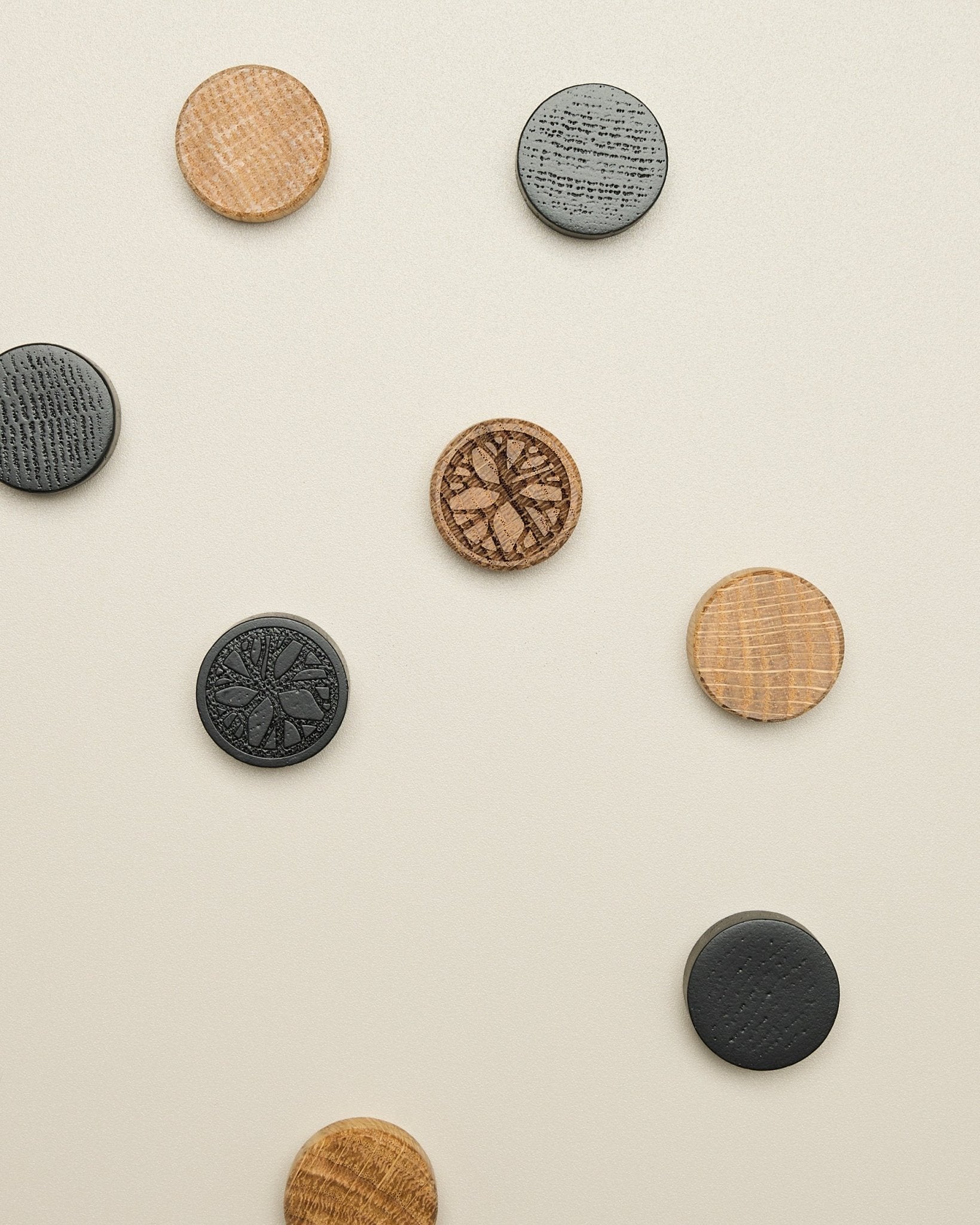 Le set d’aimants Norr de WoodUpp comprend quatre disques aux motifs natural oak et black, disposés avec soin sur une surface claire en beige ; un accessoire pour Akupanel.