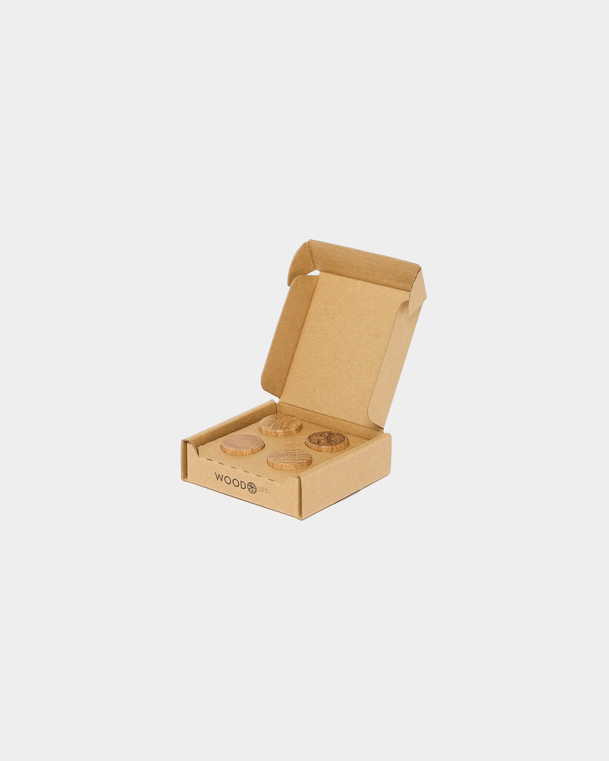 Open cardboard box containing four round wooden Akupanel accessories, placed on a white background.