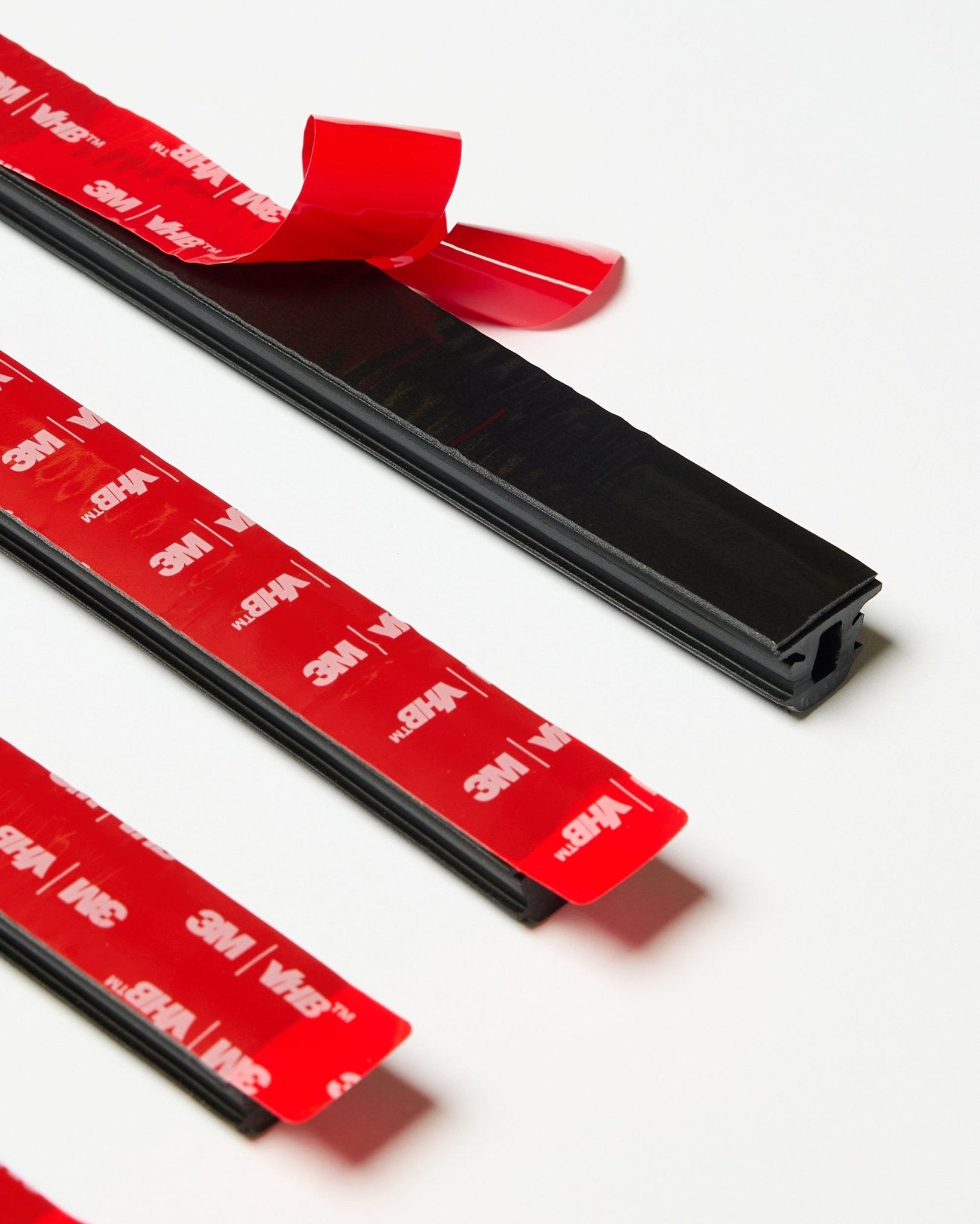 Lot de quatre bandes WoodUpp CREATE Pop-on Profile black avec support adhésif 3M rouge visible, dont une bande partiellement décollée, présenté sur une surface blanche.