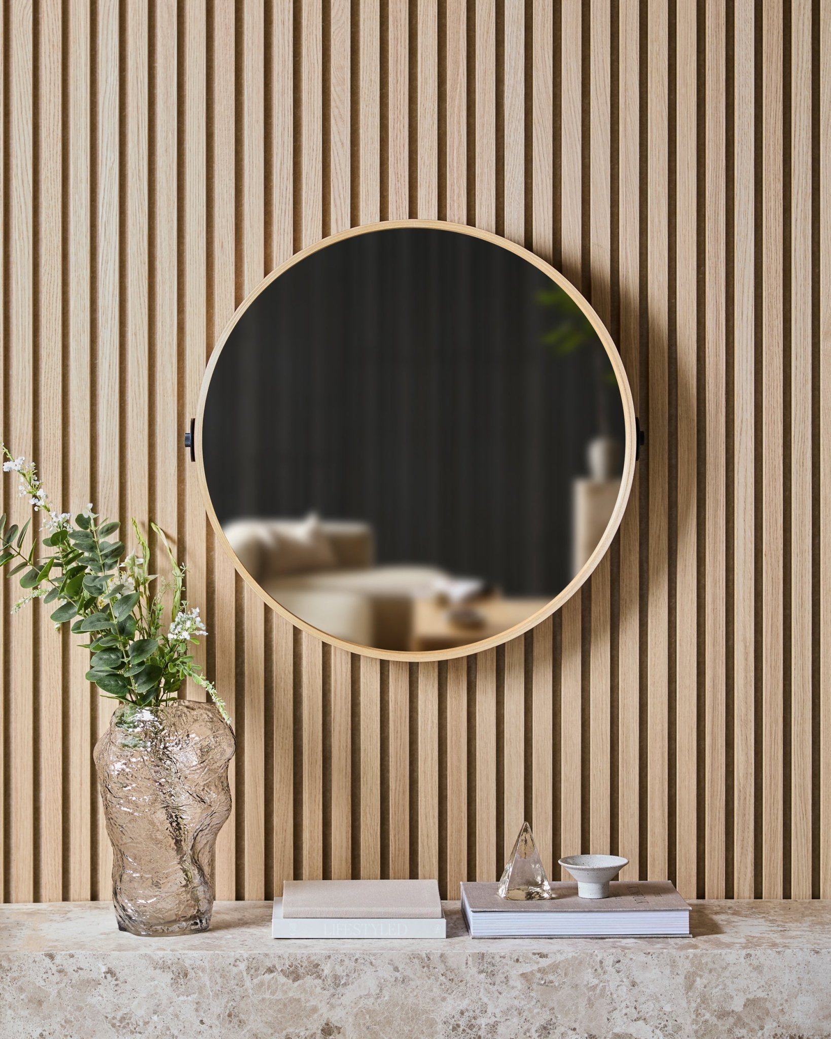 Le Linn | Mirror en Natural Oak de WoodUpp est monté sur un panneau à lattes nordique Panneau acoustique, au-dessus d’une étagère en pierre avec un vase en verre, des livres et des objets déco.