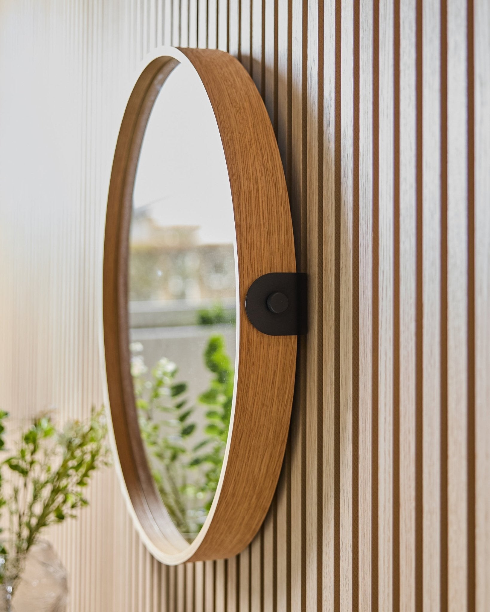 Linn | Mirror / Natural Oak de WoodUpp monté sur un mur à lattes Panneau acoustique, reflétant de la verdure et la lumière naturelle d’une fenêtre voisine.