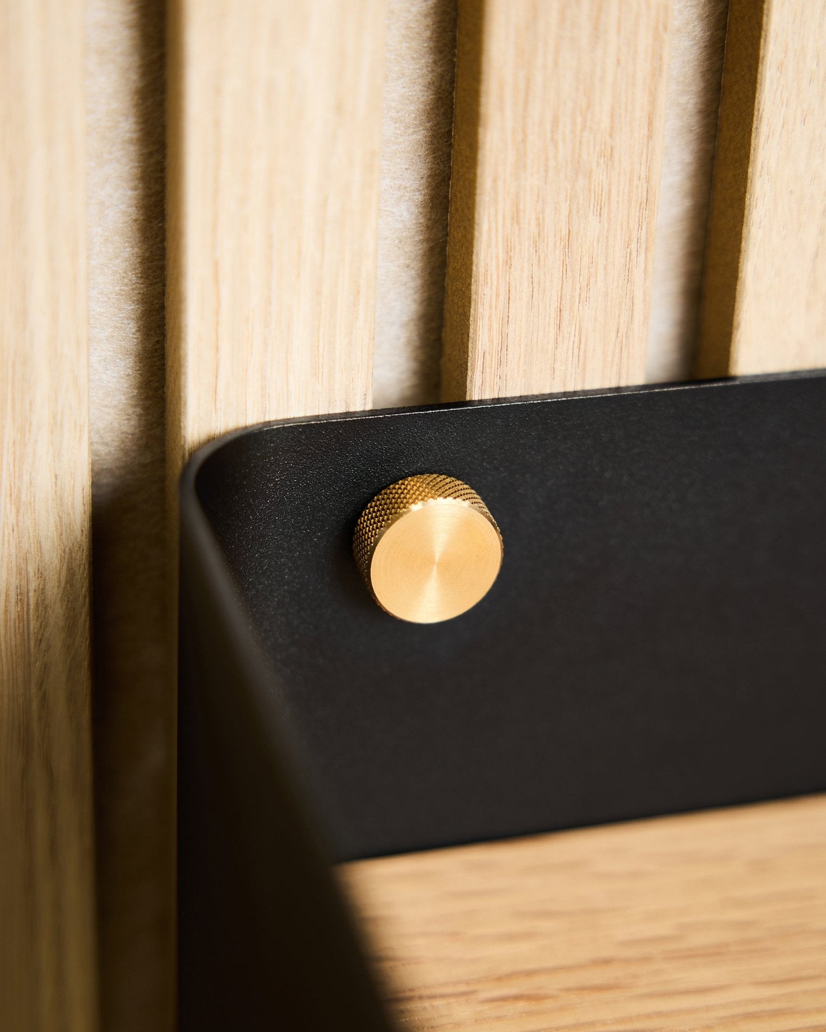 Gros plan sur deux vis moletées WoodUpp brass (M5x10 mm, 20x8.8), fixées à un support black monté sur une surface en bois nordique clair Panneau acoustique.