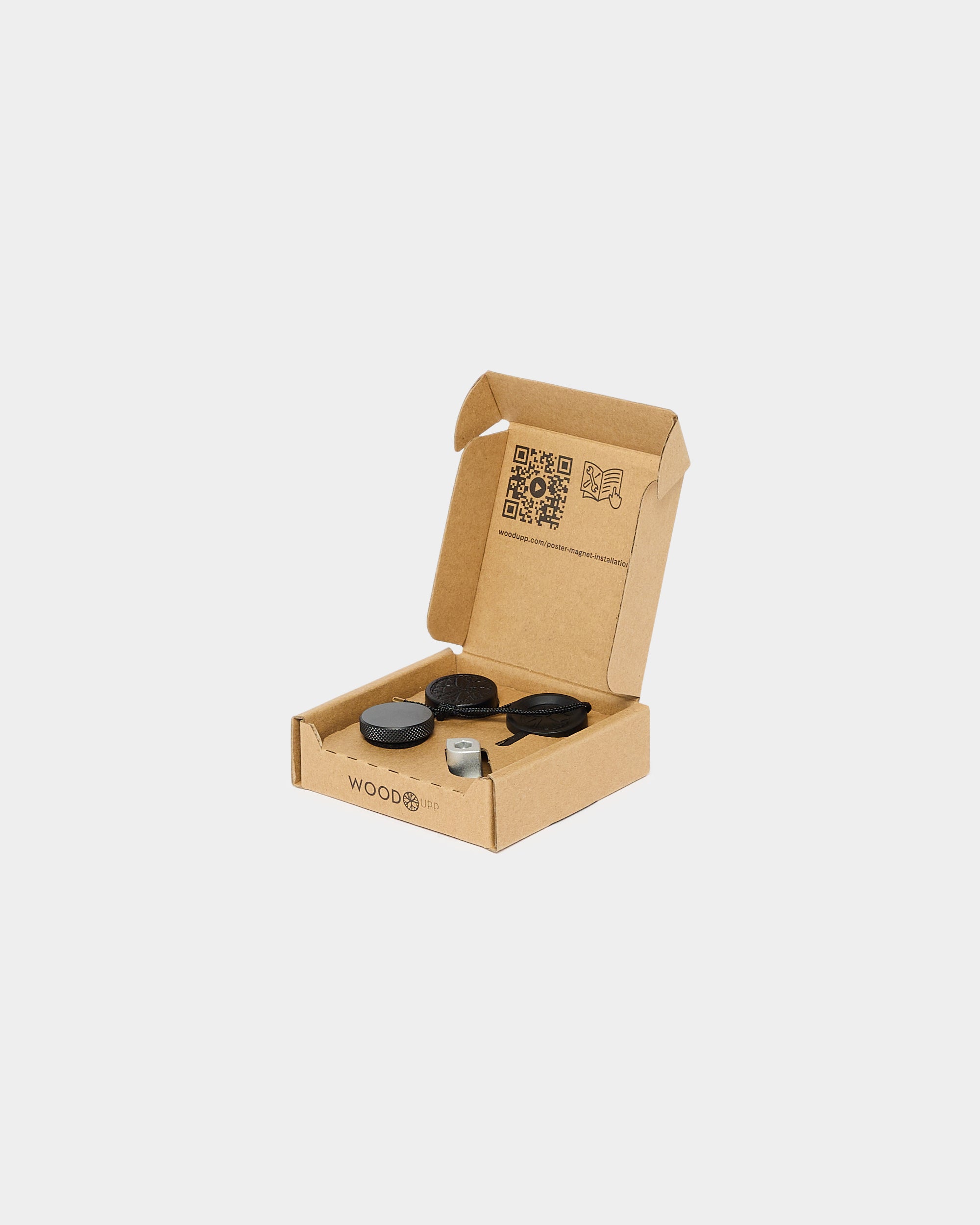 Open cardboard box containing black and white Akupanel installation components on a white background; inside lid displays printed QR codes and instructional text.