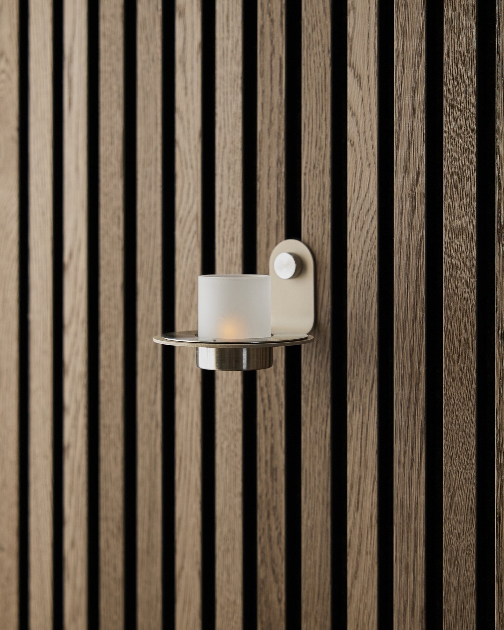 Le bougeoir Norr en acier inoxydable beige steel de WoodUpp, présenté sur un mur beige Akupanel Panneau acoustique.
