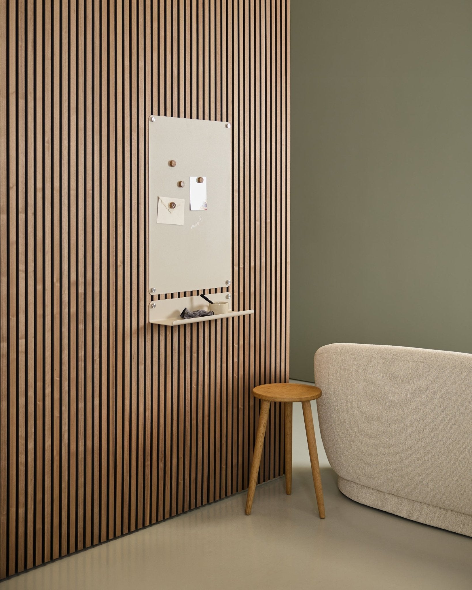 Intérieur minimaliste avec un canapé beige et un tabouret en bois, mettant en scène un tableau magnétique WoodUpp Norr large beige fixé sur un panneau acoustique en bois Nordic Akupanel, près d’un mur vert.