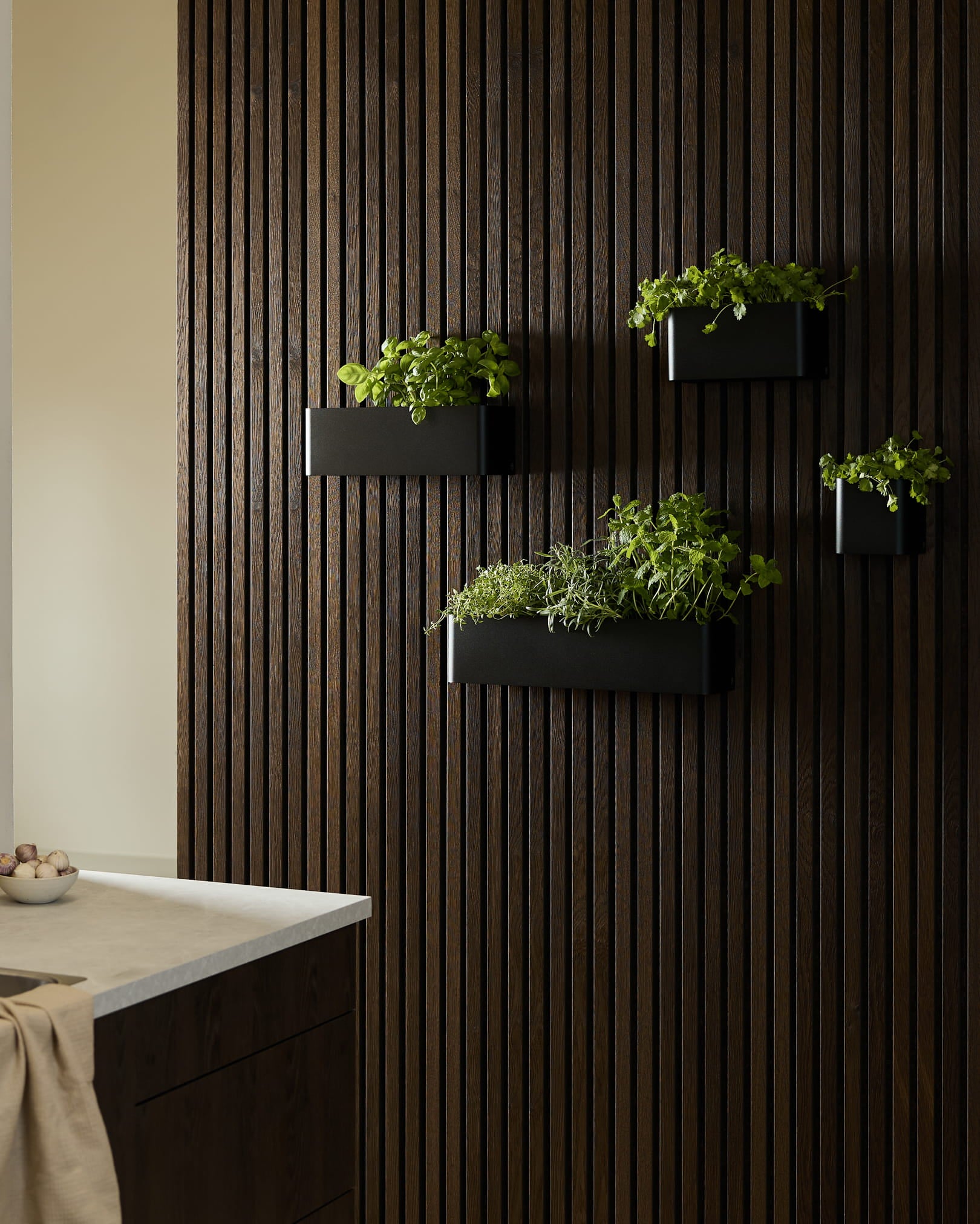 Black jardinières murales et un bac à plantes WoodUpp Norr avec des herbes vertes sur un Panneau acoustique en Akupanel bois foncé dans une cuisine moderne.