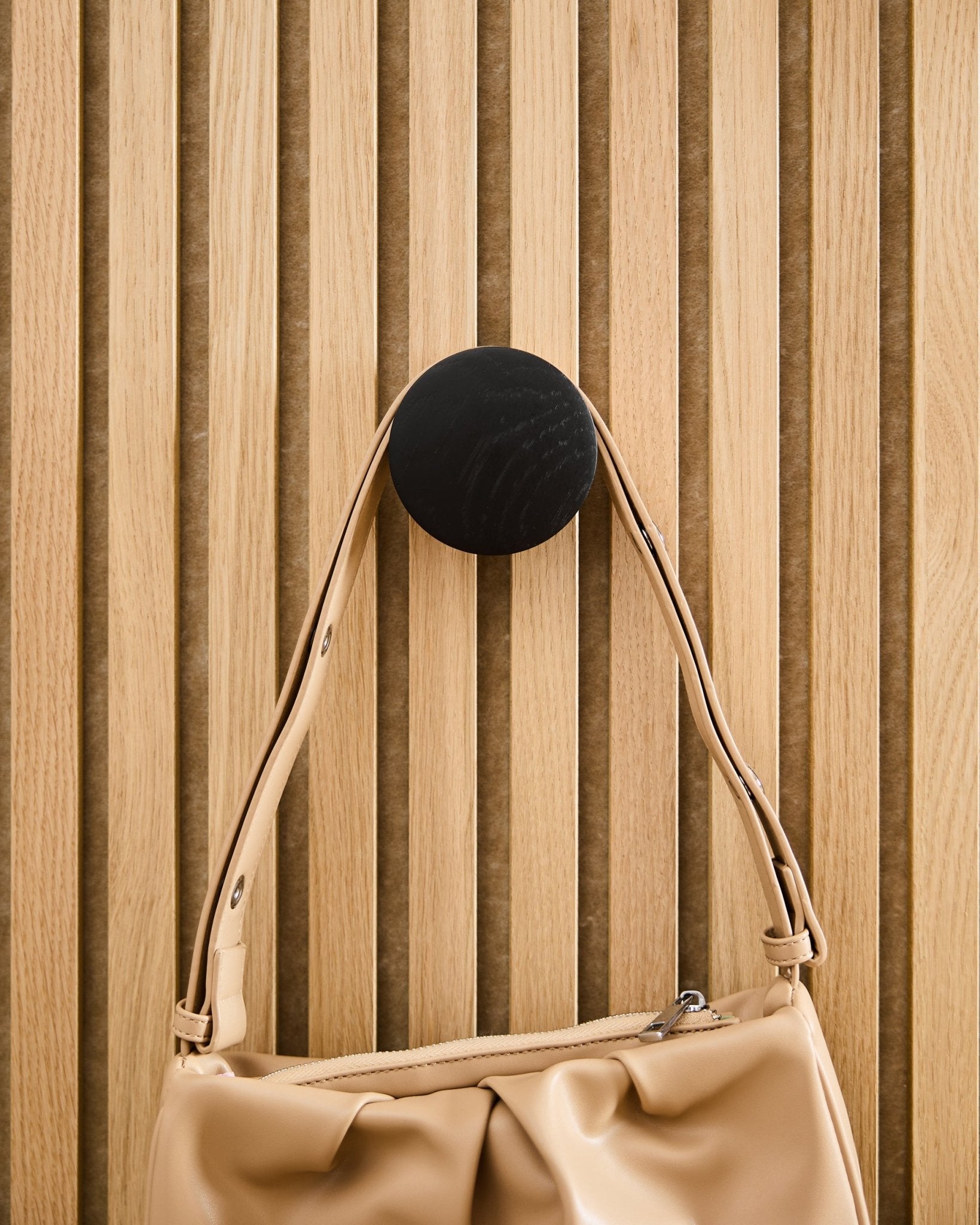Sac à main Beige suspendu à un Linn | Single Hanger WoodUpp en Black Oak, monté sur un panneau acoustique à lattes en bois clair Akupanel.