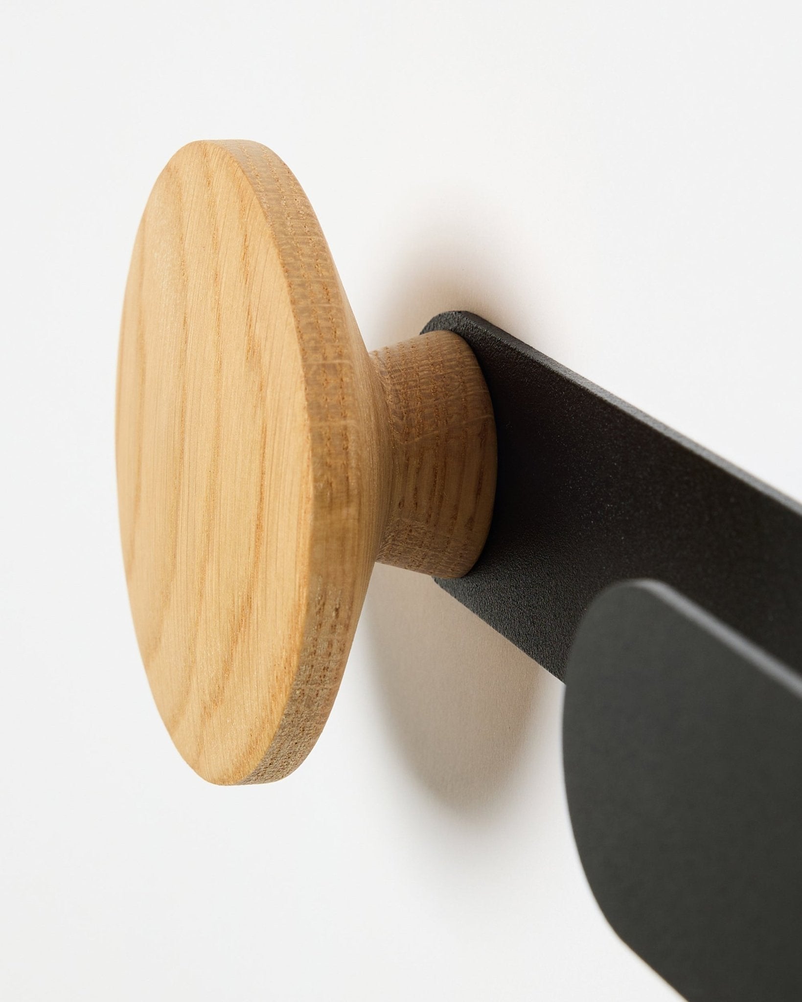 Gros plan sur le Linn Horizontal Hanger de WoodUpp en natural oak, monté sur un support métallique black, conçu pour les panneaux acoustiques Akupanel ou comme patère murale fonctionnelle.