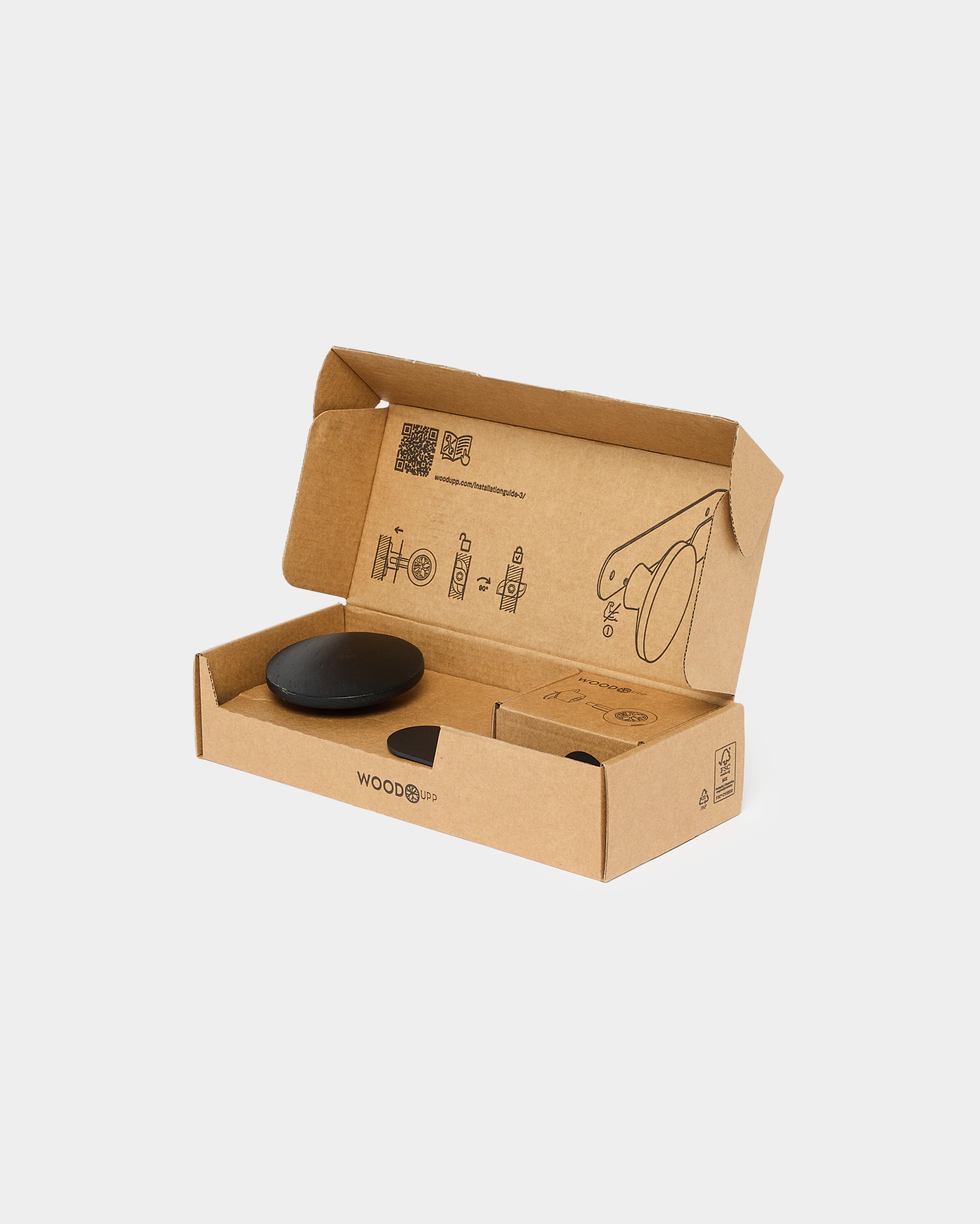 Brown cardboard packaging containing a round black mounting component and a small box, with minimalist acoustic panel assembly illustrations inside the lid.