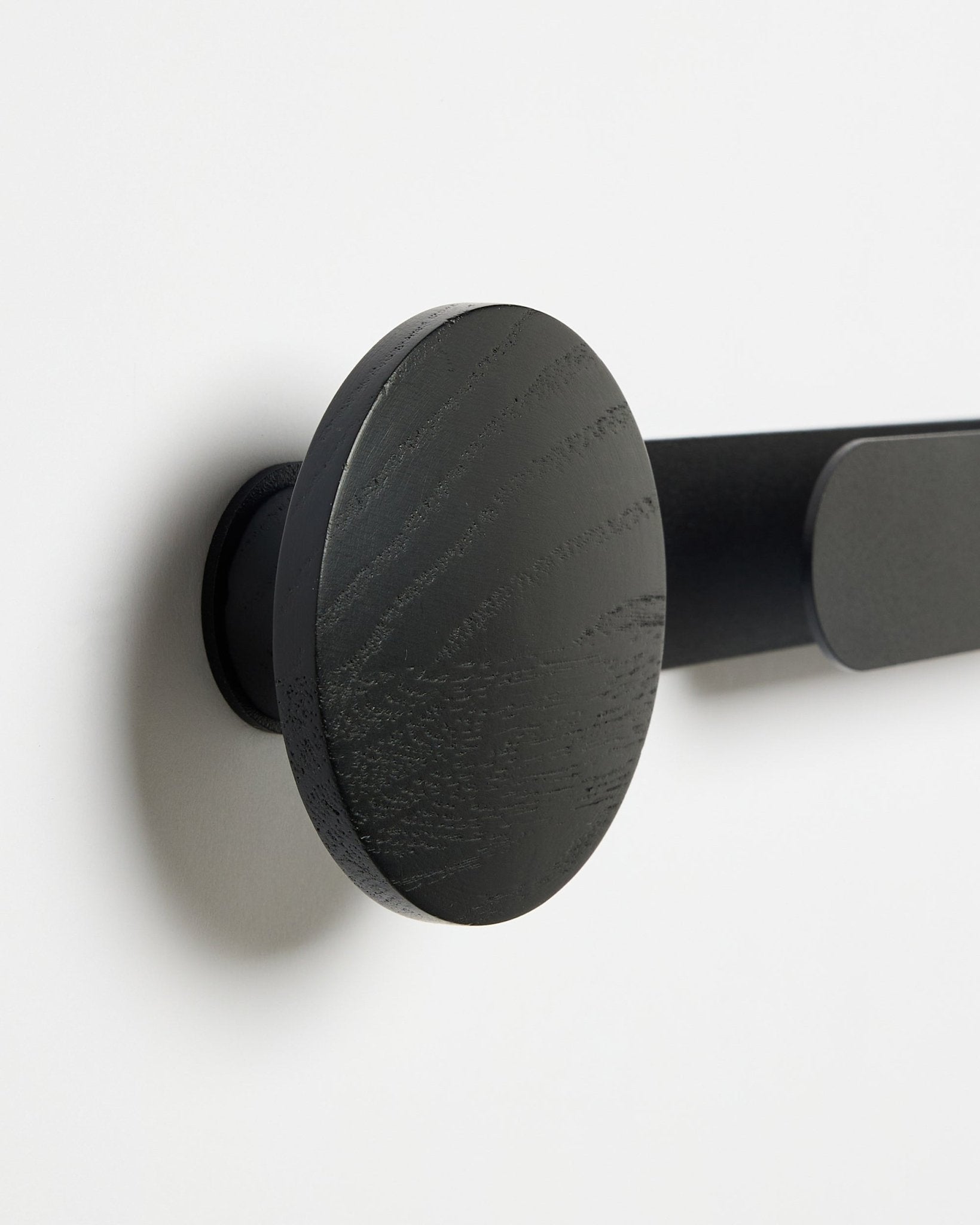 Gros plan sur le porte-manteau WoodUpp Linn | Horizontal en Black Oak, finition mate black, monté sur un mur blanc ; accessoire pour panneaux acoustiques en bois.
