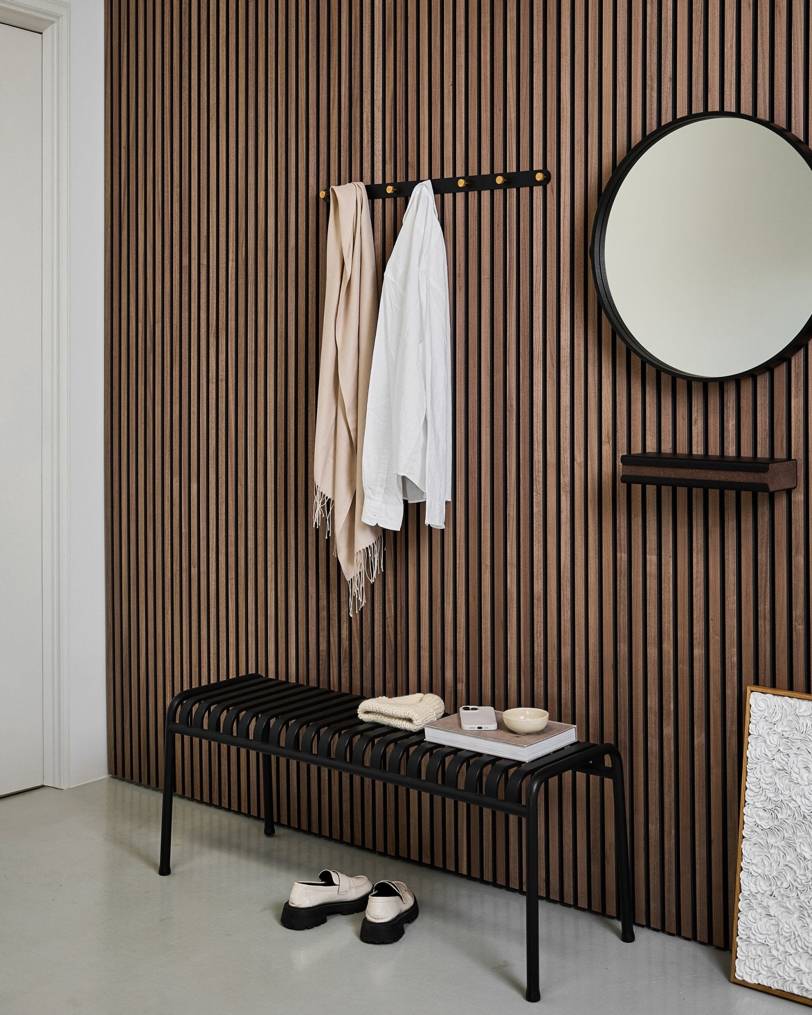 Entrée minimaliste avec un mur acoustique à lattes WoodUpp Akupanel, un porte-manteau mural Norr (Black/Brass, X7), un banc, un miroir et une décoration moderne aux tons neutres.