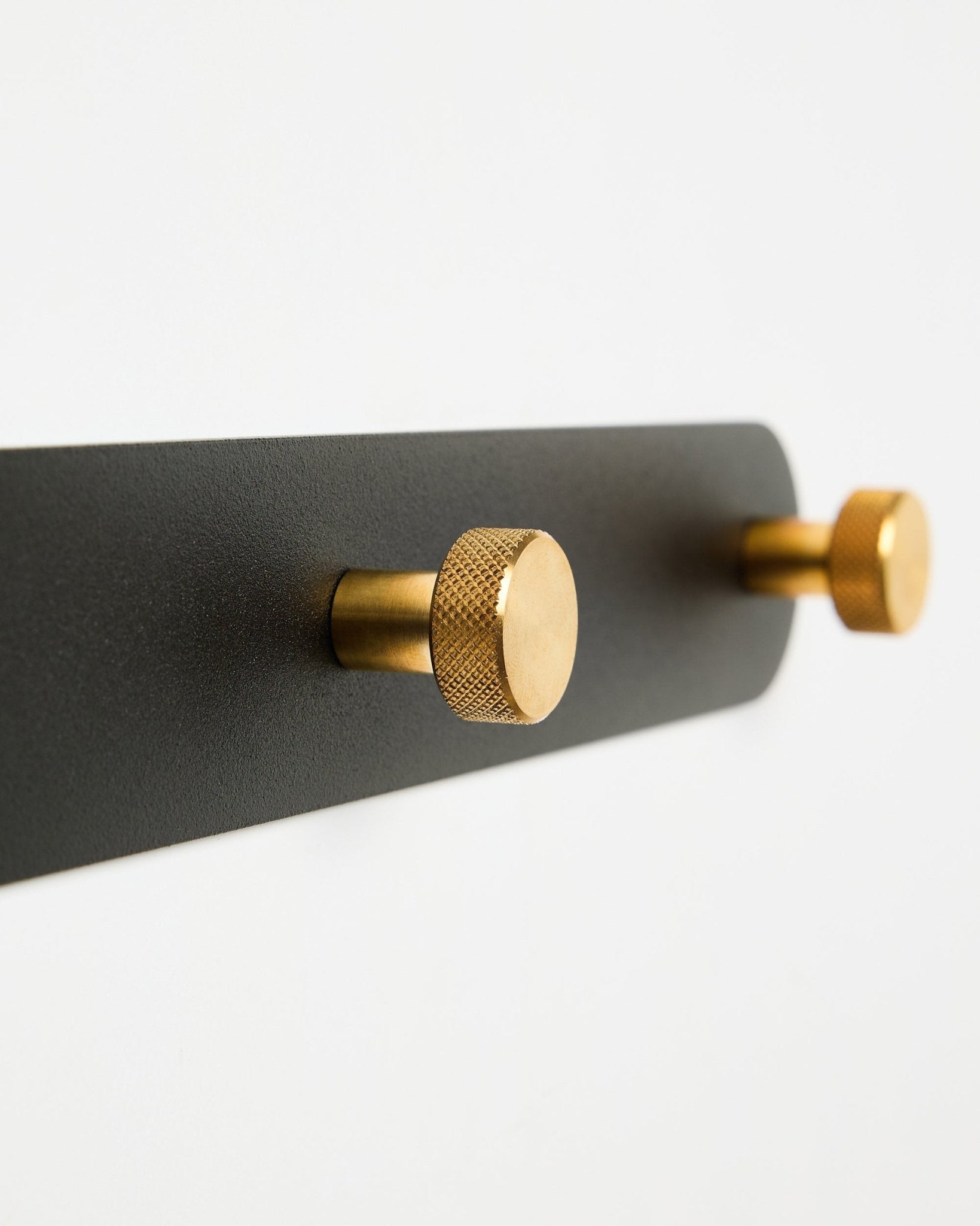 Porte-manteau mural WoodUpp Norr, modèle X7, avec deux crochets cylindriques black et brass sur un support black, présenté sur fond blanc.
