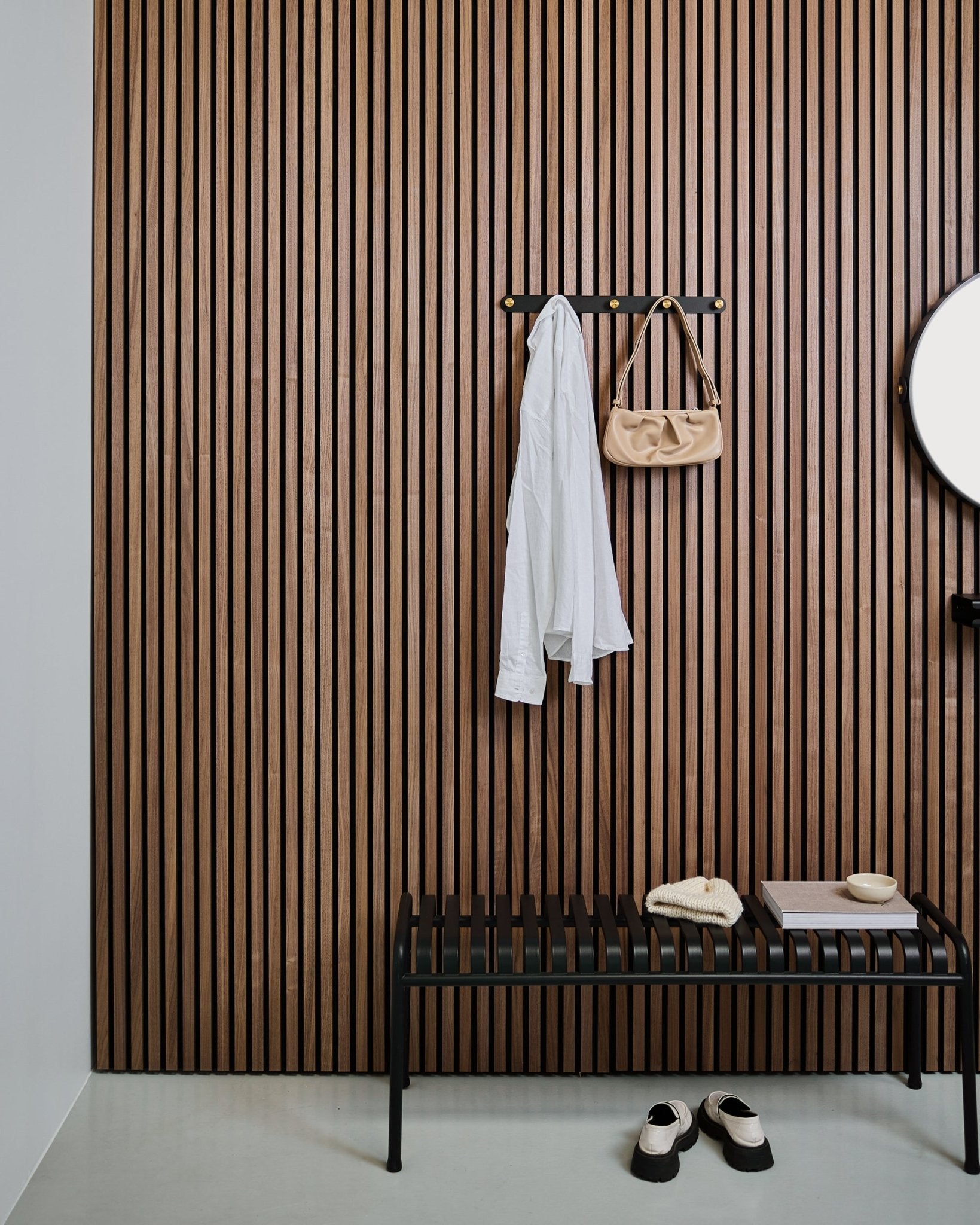 Le porte-manteau WoodUpp Norr en black et brass porte une chemise blanche et un sac beige au-dessus d’un banc black ; des chaussons blancs sont rangés avec soin en dessous.