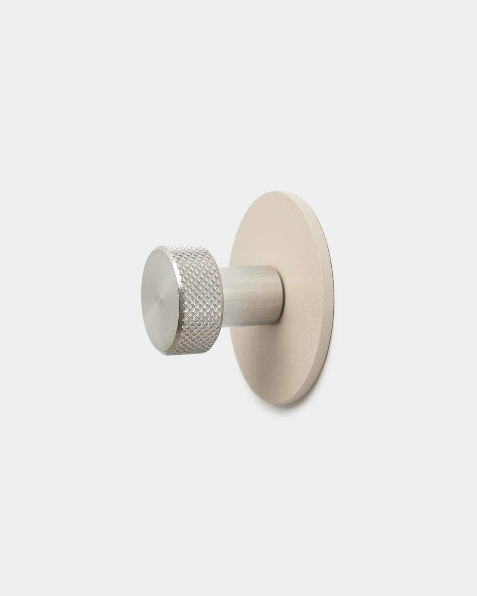 Patère WoodUpp Norr en beige et acier inoxydable steel, avec une extrémité cylindrique texturée et une base ronde, accessoire pour Akupanel, sur fond blanc uni.
