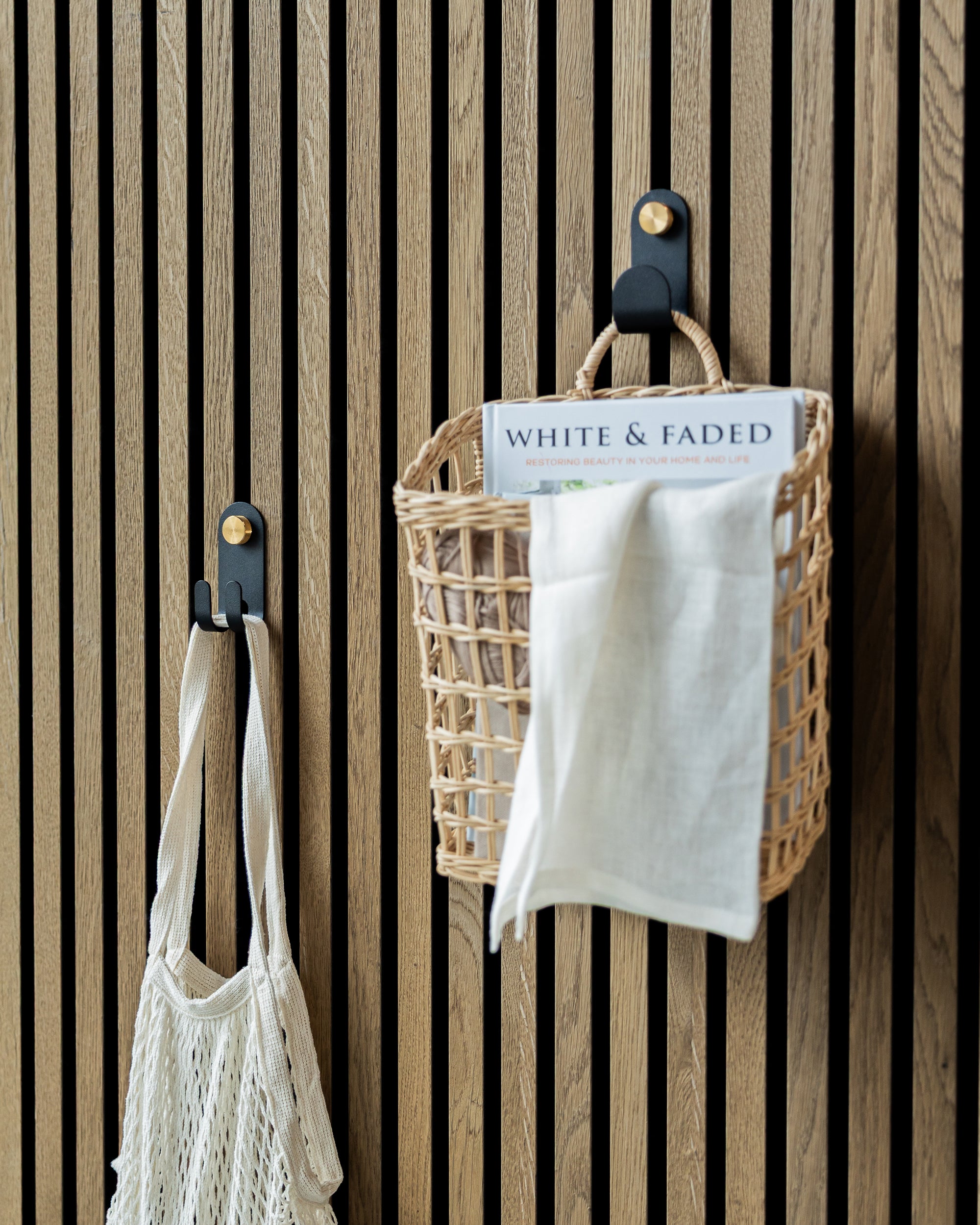 A mesh bag and a woven basket with a magazine and cloth hang on hooks mounted to vertical acoustic slatwall panels.