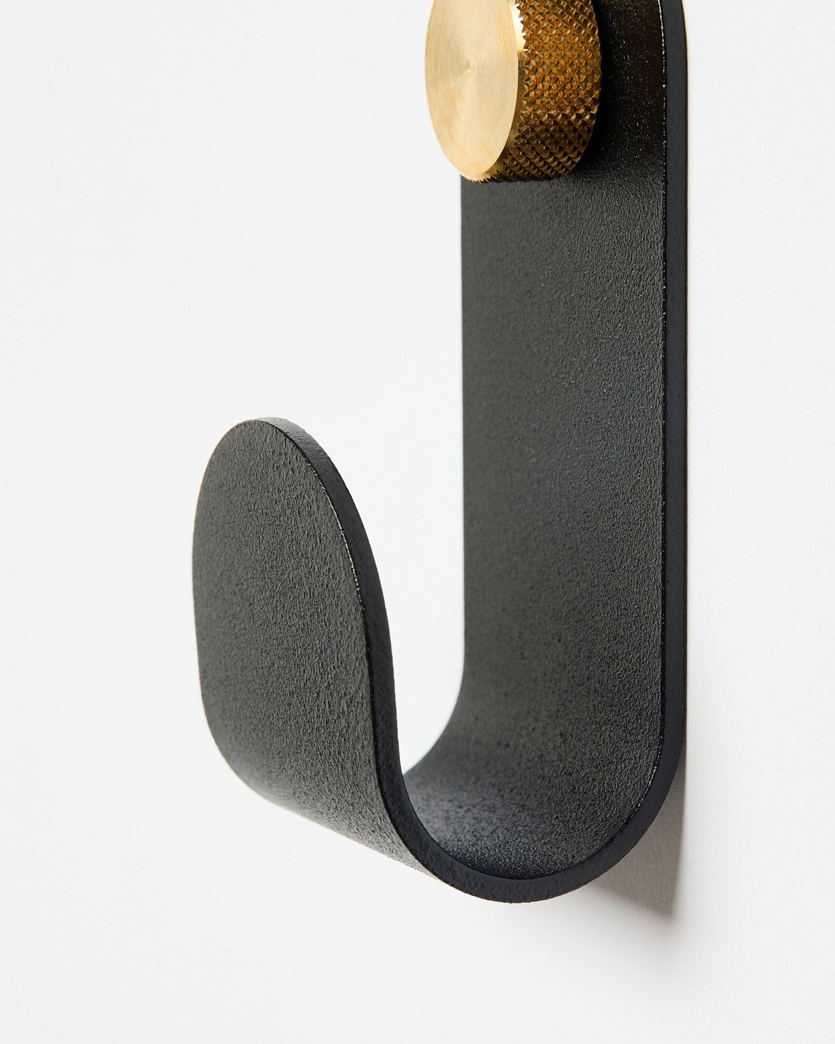 Le Norr Single Hanger de WoodUpp présente un bras courbé en métal black avec un embout doré, conçu comme accessoire à utiliser avec des panneaux acoustiques sur des murs blancs.