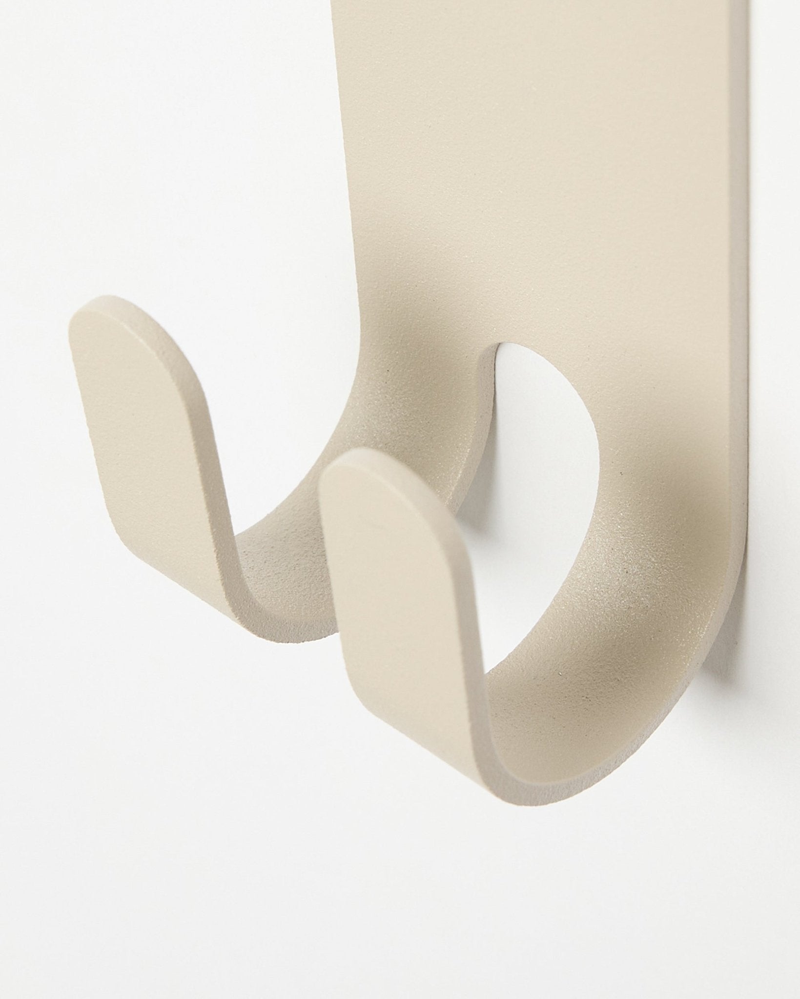 Gros plan sur le Norr Double Hanger en beige de WoodUpp, un crochet mural minimaliste en métal installé sur un Panneau acoustique colored clair à lattes.