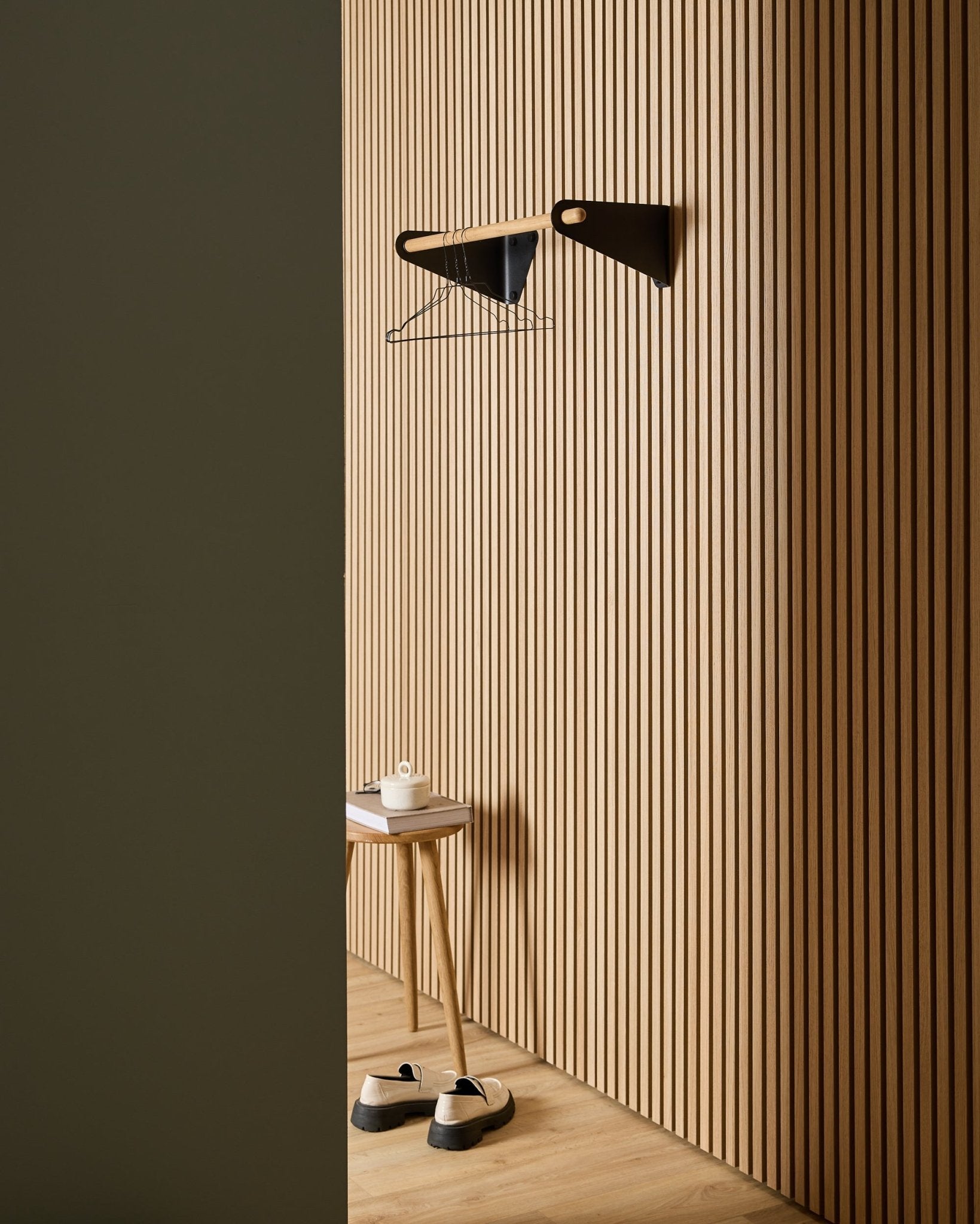 Entrée minimaliste avec panneaux acoustiques muraux à lattes en bois Nordic WoodUpp Akupanel, porte-manteau black Linn (75,9 cm), tabouret, chaussures, étagère murale et rouleau de papier.