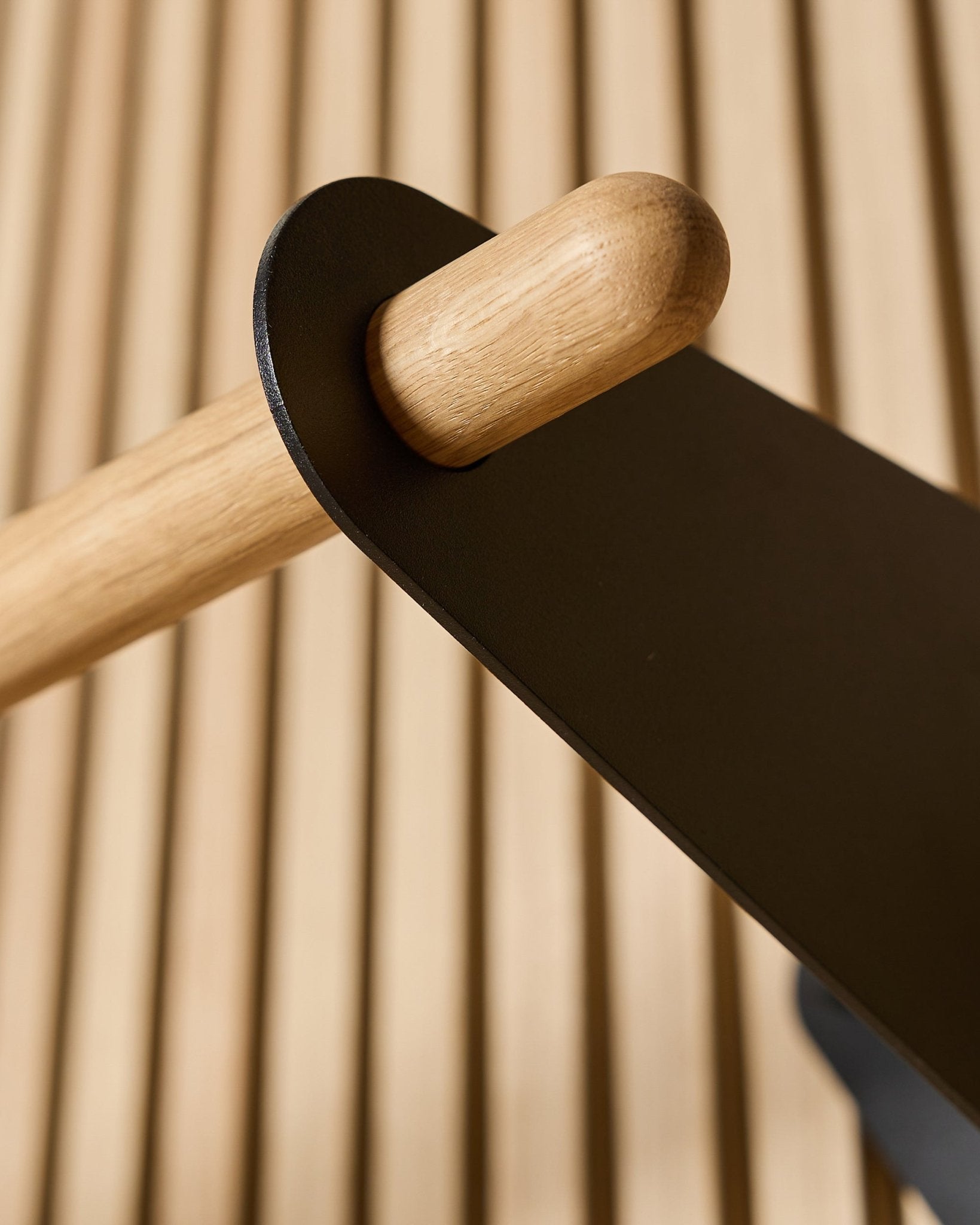 Gros plan sur le porte-manteau WoodUpp Linn en black, 75,9 cm, avec une tige en chêne massif montée sur un support métallique black, fixée à un panneau acoustique mural à lattes Nordic.