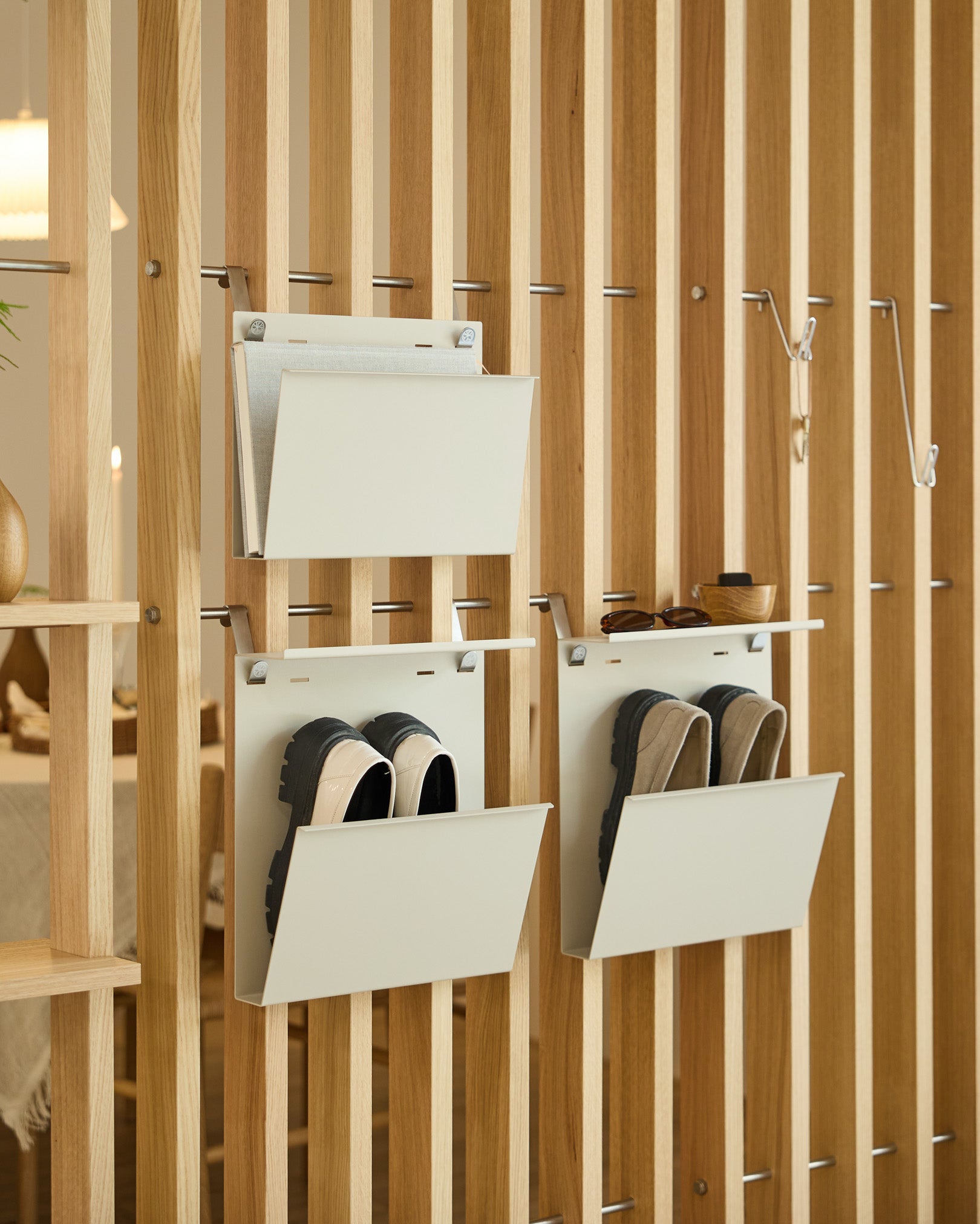 Le porte-revues Nell de WoodUpp en beige est fixé à un séparateur de pièce en vertical, offrant un rangement organisé pour les magazines et les objets small.