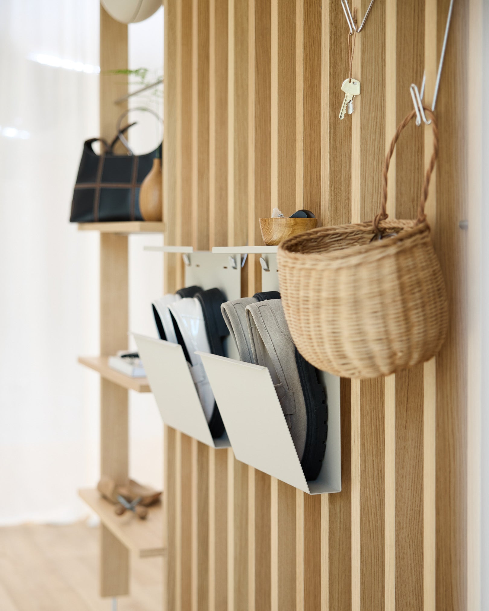 Entrée moderne avec le rangement à chaussures Nell de WoodUpp en beige, des murs en panneaux acoustiques en bois Akupanel, des patères murales, un panier suspendu et une étagère présentant des objets déco.