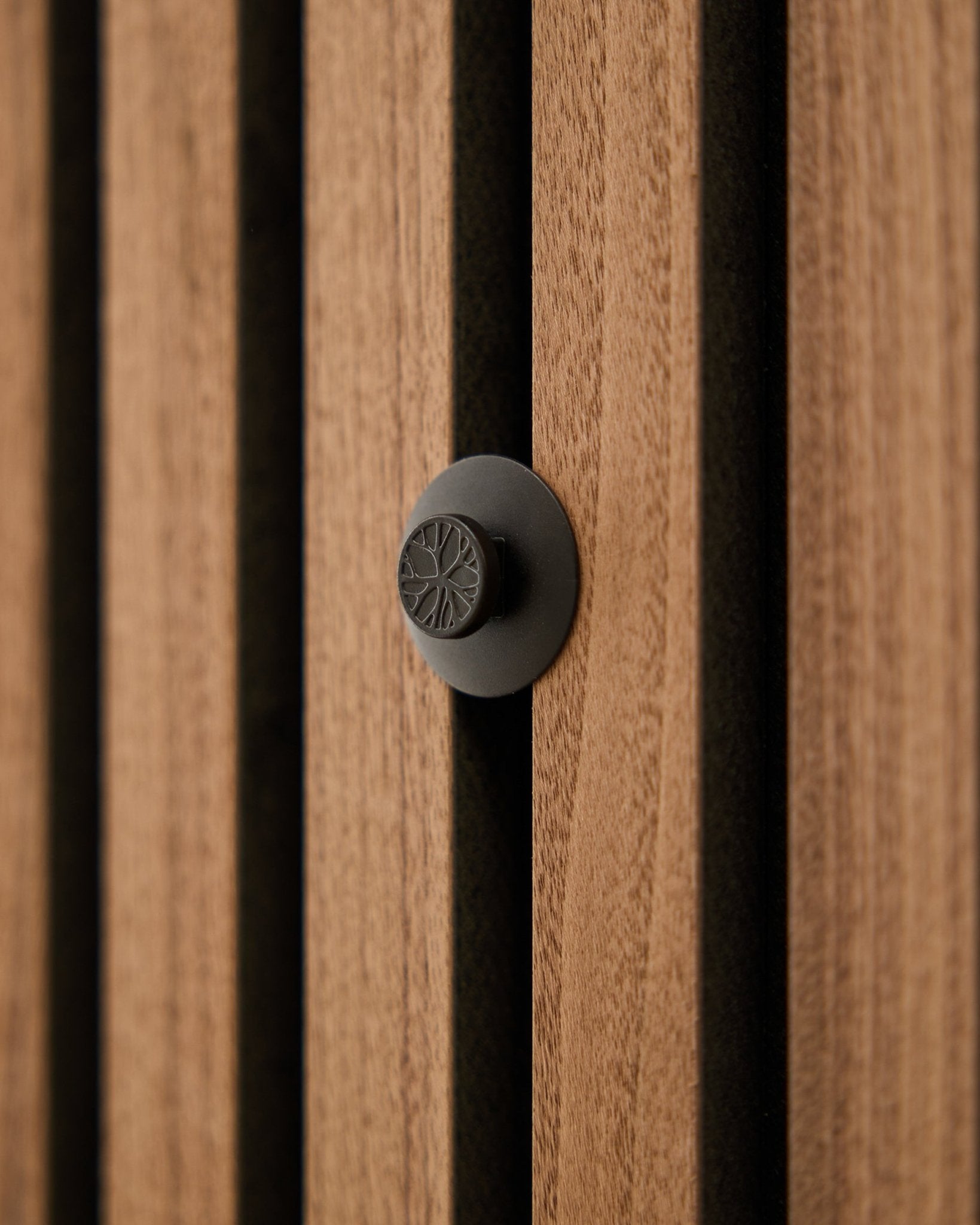 Gros plan sur un bouton rond black du set WoodUpp Dupps Original, installé sur un mur acoustique moderne en tasseaux de bois vertical Akupanel.