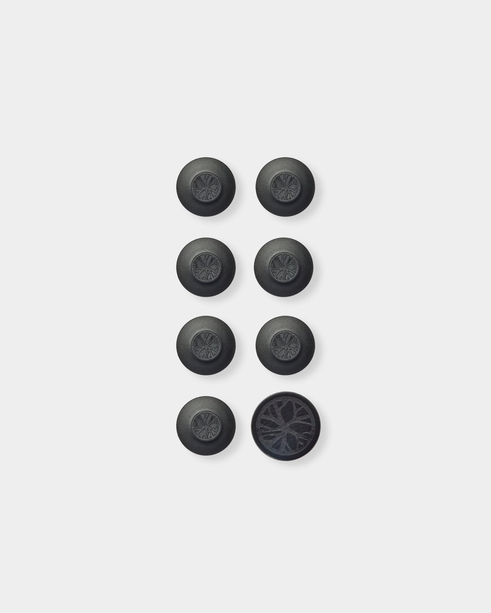Sept accessoires ronds black Dupps Panneau acoustique de WoodUpp et un outil disposés en grille ; en bas à droite, un Dupp retourné pour montrer son dessous texturé.