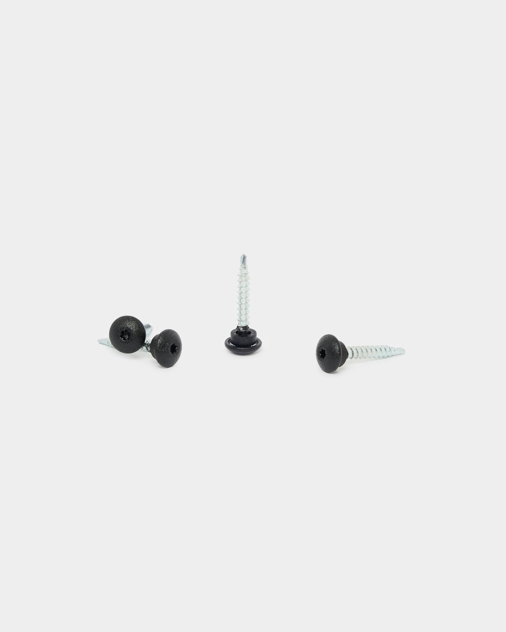 Trois vis black WoodUpp 4,8x35 avec rondelles Ø9,5 sur fond blanc, conçues comme fixations pour les panneaux de façade extérieurs Aluwood.