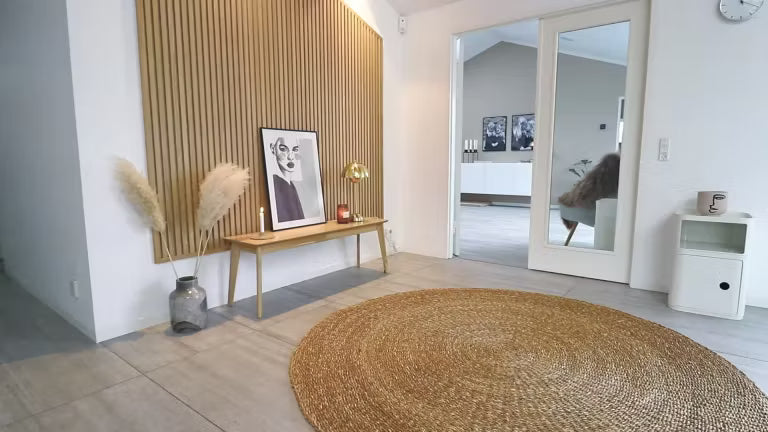Espace de vie nordique minimal avec un tapis rond en jute, un banc en bois contenant de lherbe de la pampa, des œuvres dart encadrées et un mur daccent en bois acoustique Akupanel à lattes.