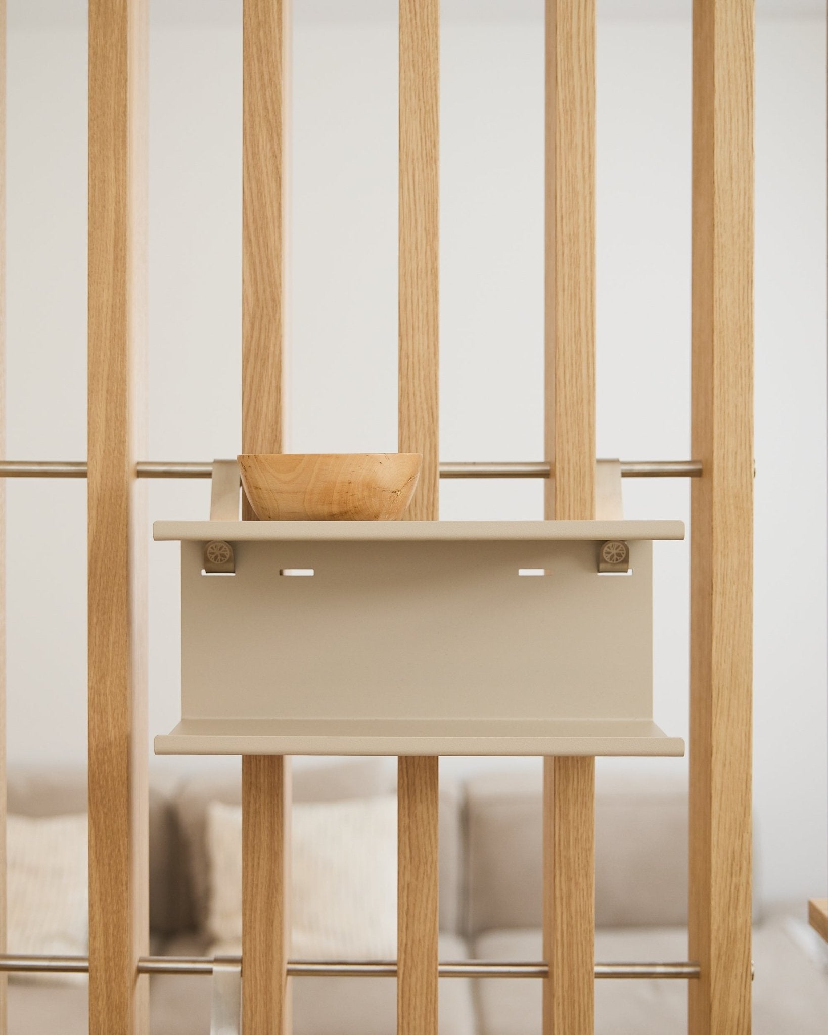 Un bol en bois small sur l’étagère métallique double Nell beige de WoodUpp (31,7 cm), avec un canapé et des coussins flous en arrière-plan.