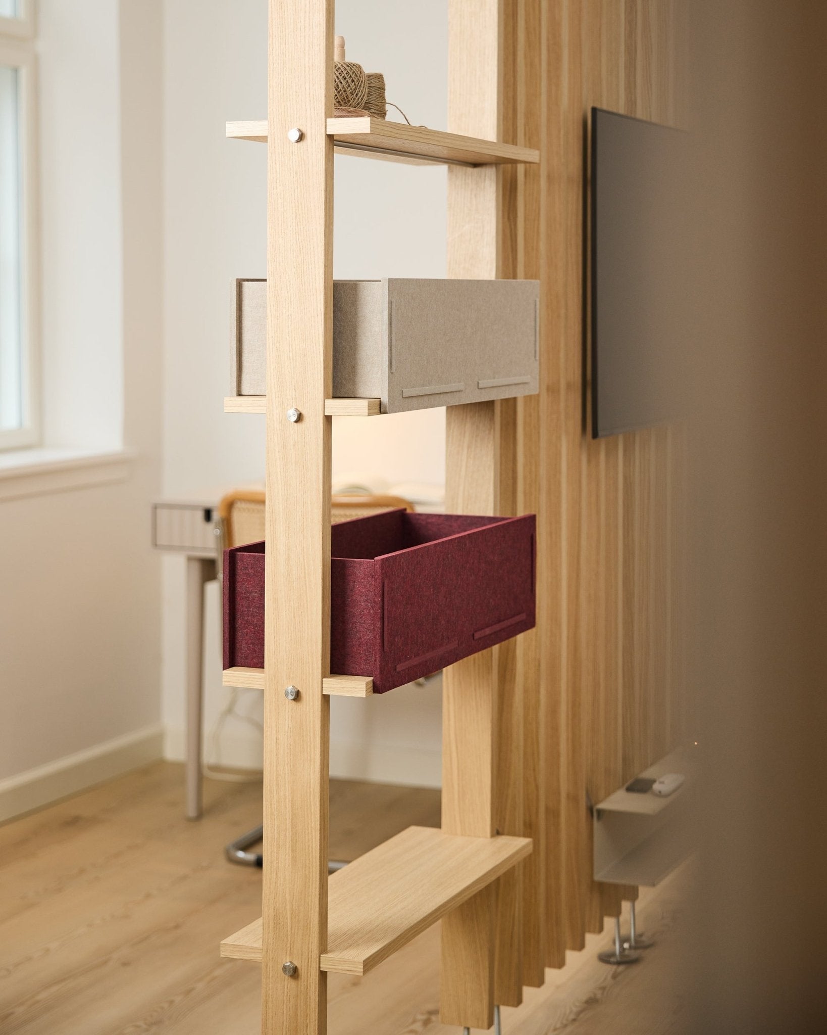 Une étagère WoodUpp présente une boîte de rangement beige et une Vigg Felt Box ox red / BM2 dans une pièce nordique lumineuse et minimaliste, avec des détails acoustiques en bois.