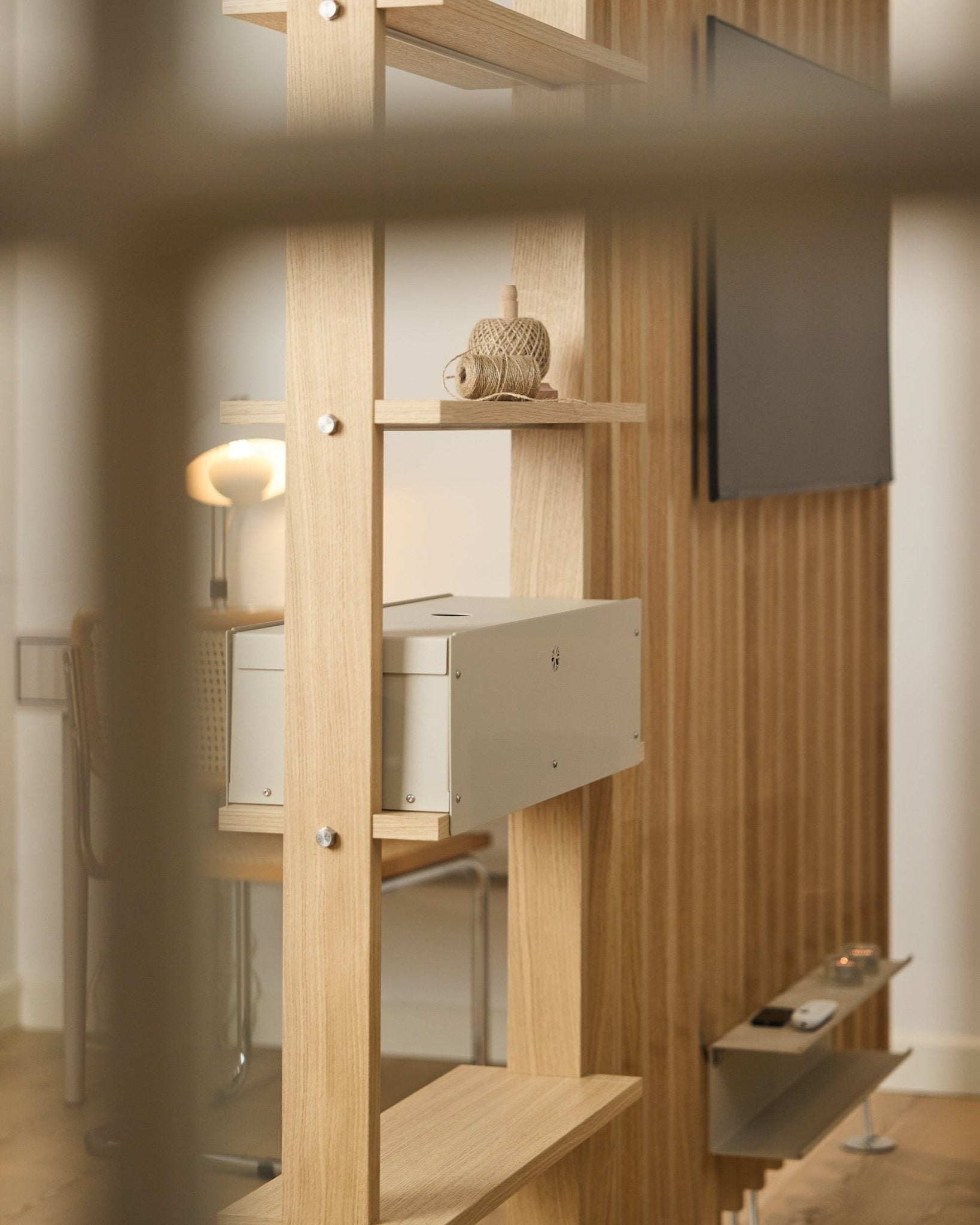 Une pièce chaleureuse avec une chaise, une lampe et une TV met en scène l’étagère Nell | Metal Box / BM2 de WoodUpp, dans une finition beige, avec une décoration nordique minimaliste.