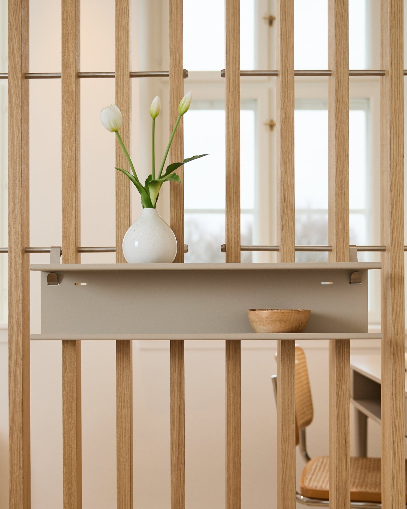 Double Metal Shelf / BM1 de WoodUpp en beige (63,5 cm), montée sur un séparateur de pièce à lames, mise en scène avec un vase et un bol en bois.
