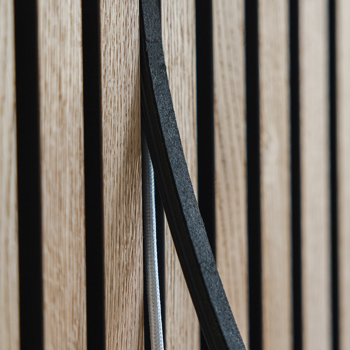 Close-up of Akupanel acoustic wood slats with black gaps and a curved edge, featuring a visible white cable running vertically along the panel.