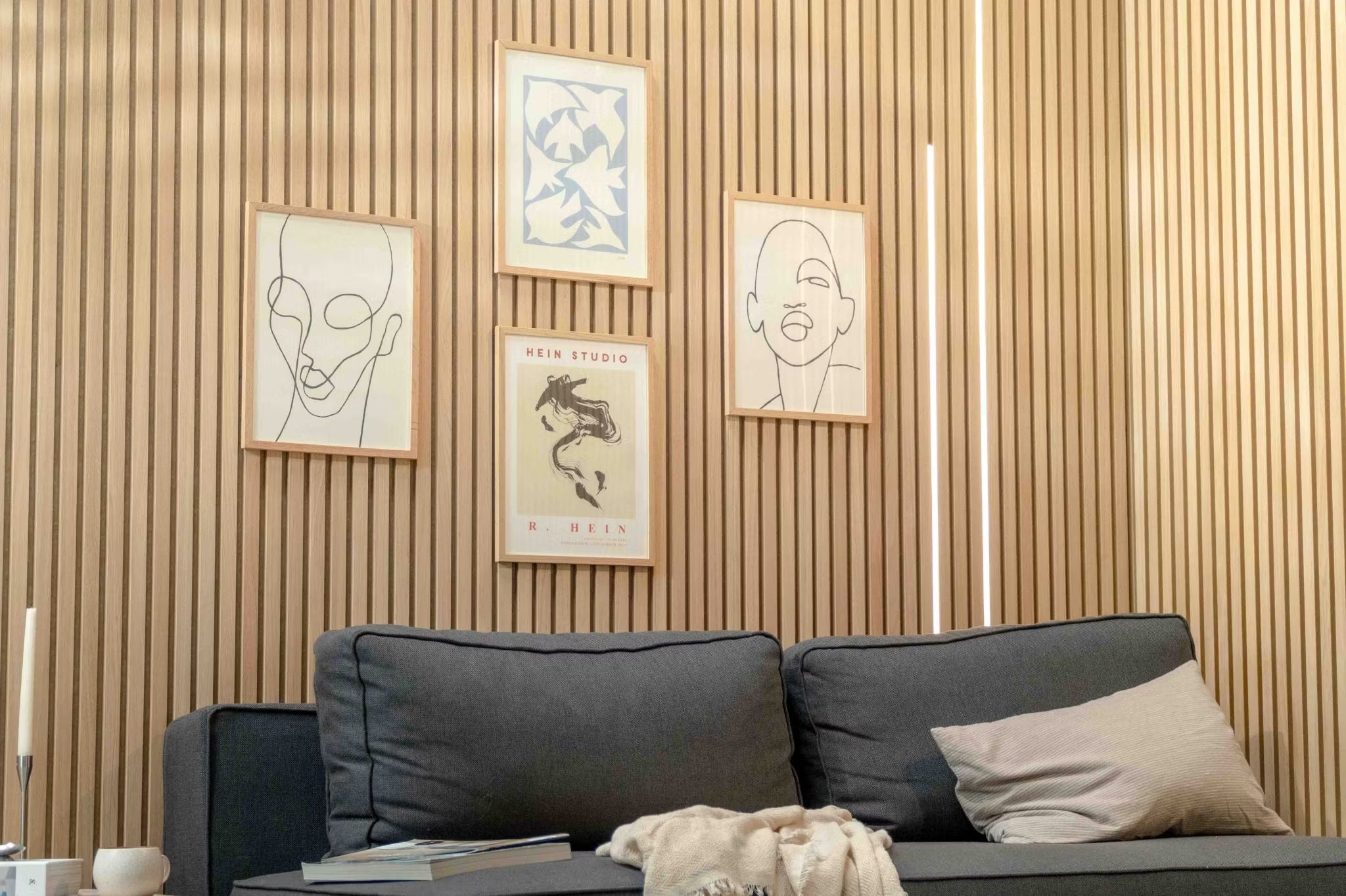 Salon moderne composé dun canapé foncé avec un coussin beige, accentué par un mur de lattes en bois acoustique Akupanel et un art scandinave minimaliste au-dessus.
